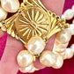 Close-up of gold-tone sculptural clasp with domed faux pearl on a vintage YSL pearl necklace, held in hand to show detail and hallmark