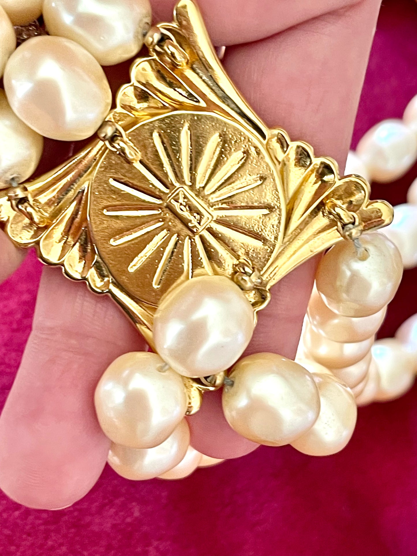 Close-up of gold-tone sculptural clasp with domed faux pearl on a vintage YSL pearl necklace, held in hand to show detail and hallmark