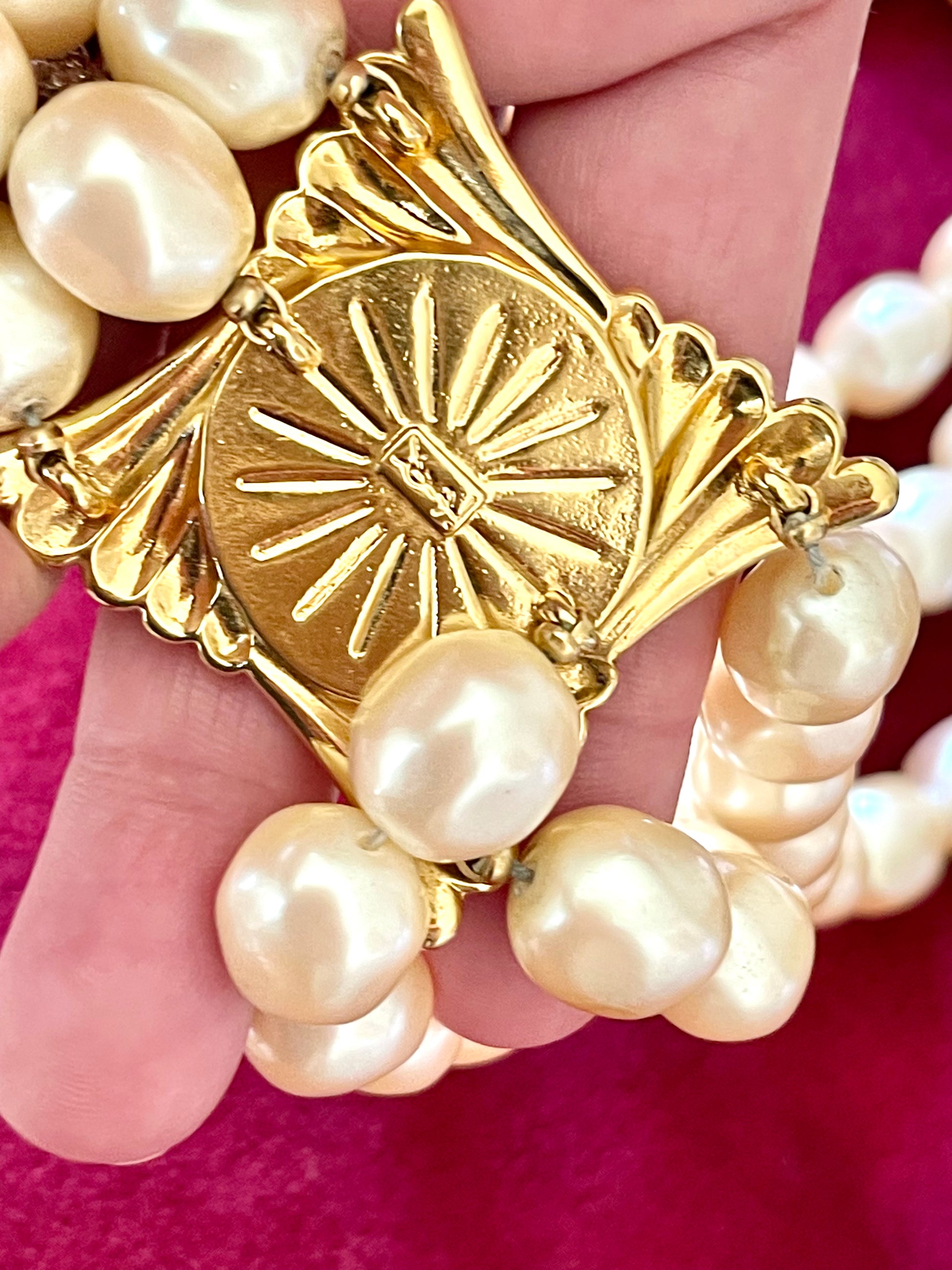 Close-up of gold-tone sculptural clasp with domed faux pearl on a vintage YSL pearl necklace, held in hand to show detail and hallmark