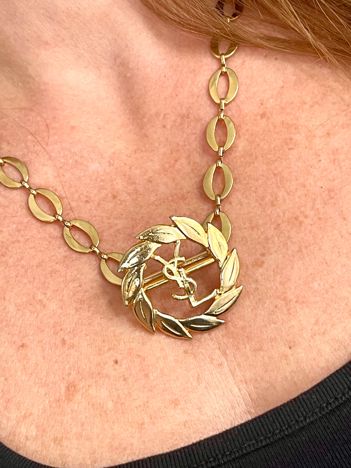 Close-up of a person wearing a refurbished vintage YSL laurel wreath pendant mounted on a gold-plated stainless steel necklace