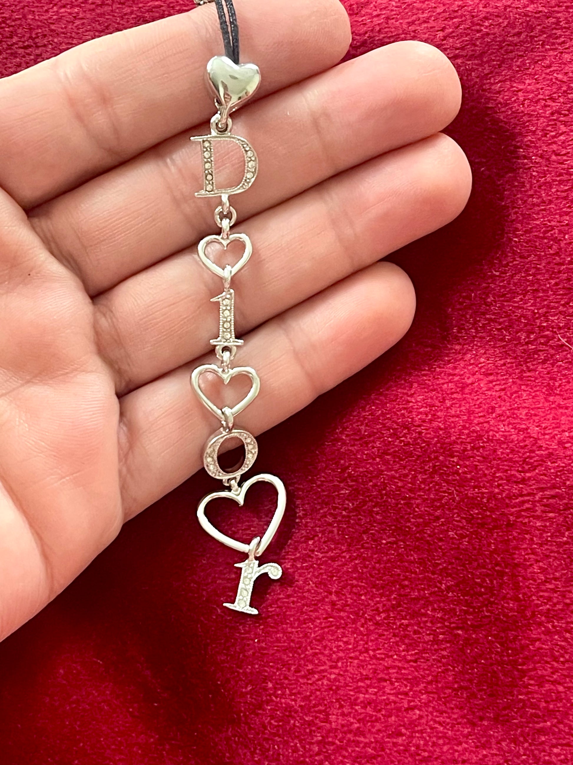 Close-up of Dior phone charm pendant with silver beads and clasp detail, highlighting one-of-a-kind design placed on hand 