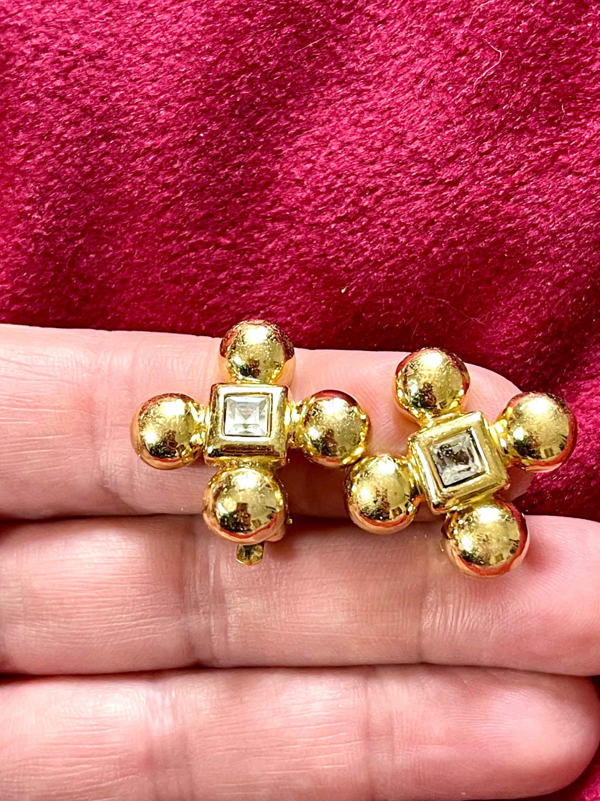 Yves Saint Laurent vintage gold tone cross clip-on earrings from the 1980s held in hand, showing rounded gold domes and square-cut center stones