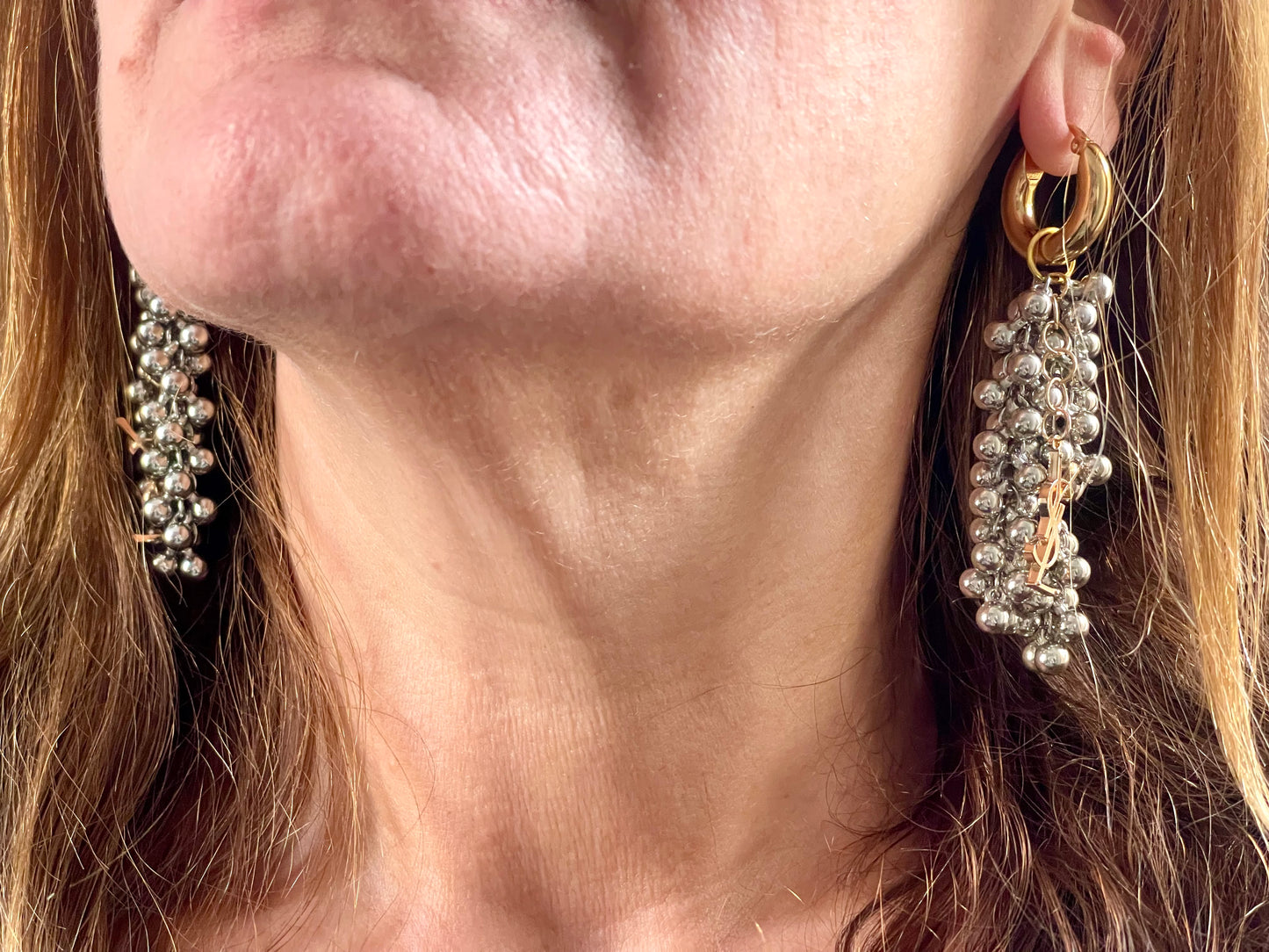 Over view of a pair of Gold and silver earrings with pearl-like beads and YSL Yves Saint Laurent charms worn by model