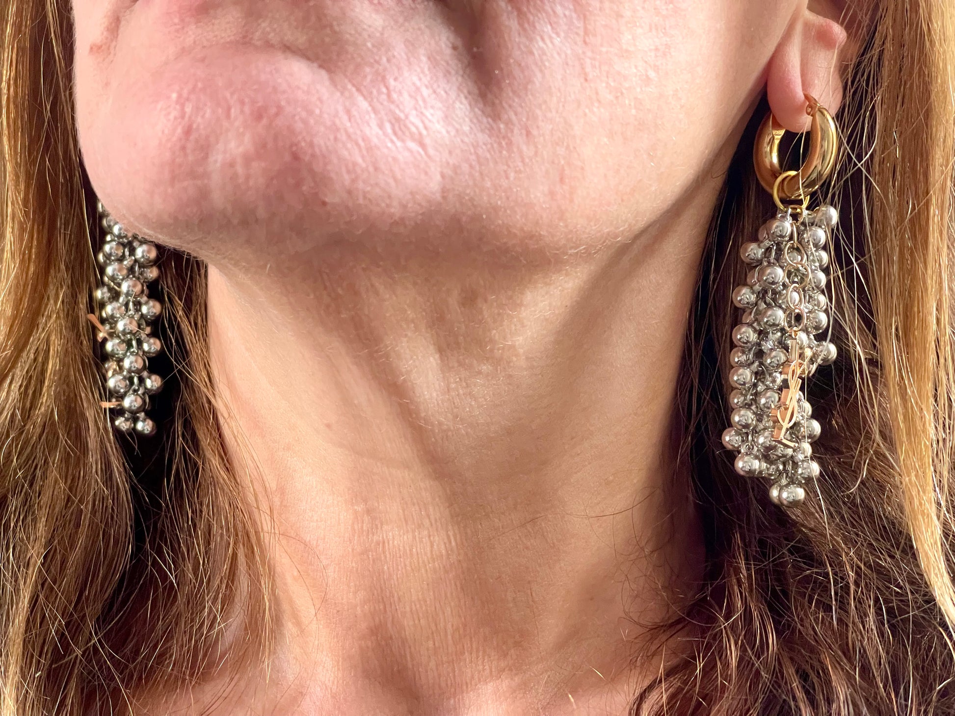 Over view of a pair of Gold and silver earrings with pearl-like beads and YSL Yves Saint Laurent charms worn by model