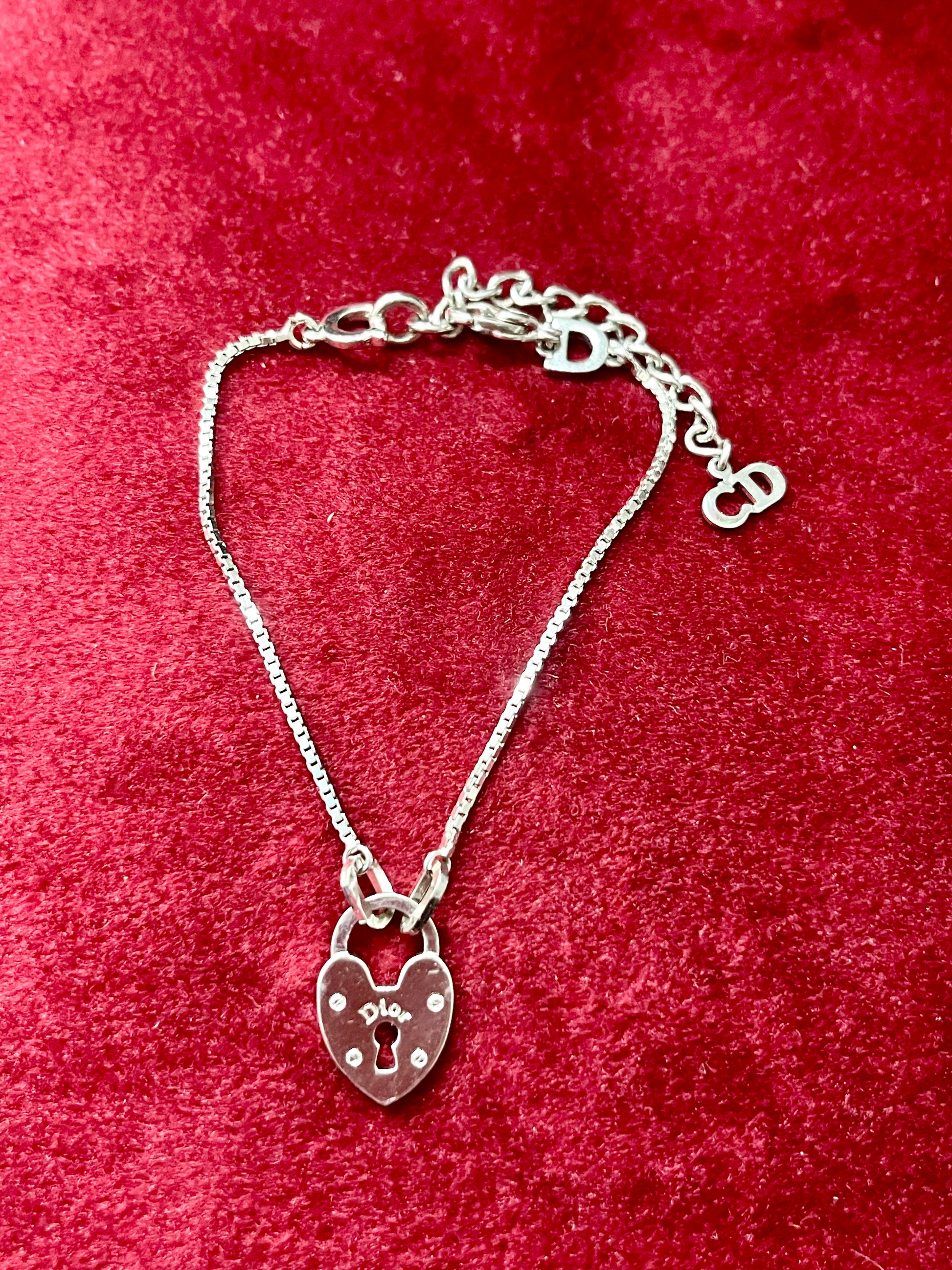 Silver bracelet Dior with a heart-shaped lock charm on a red textured background