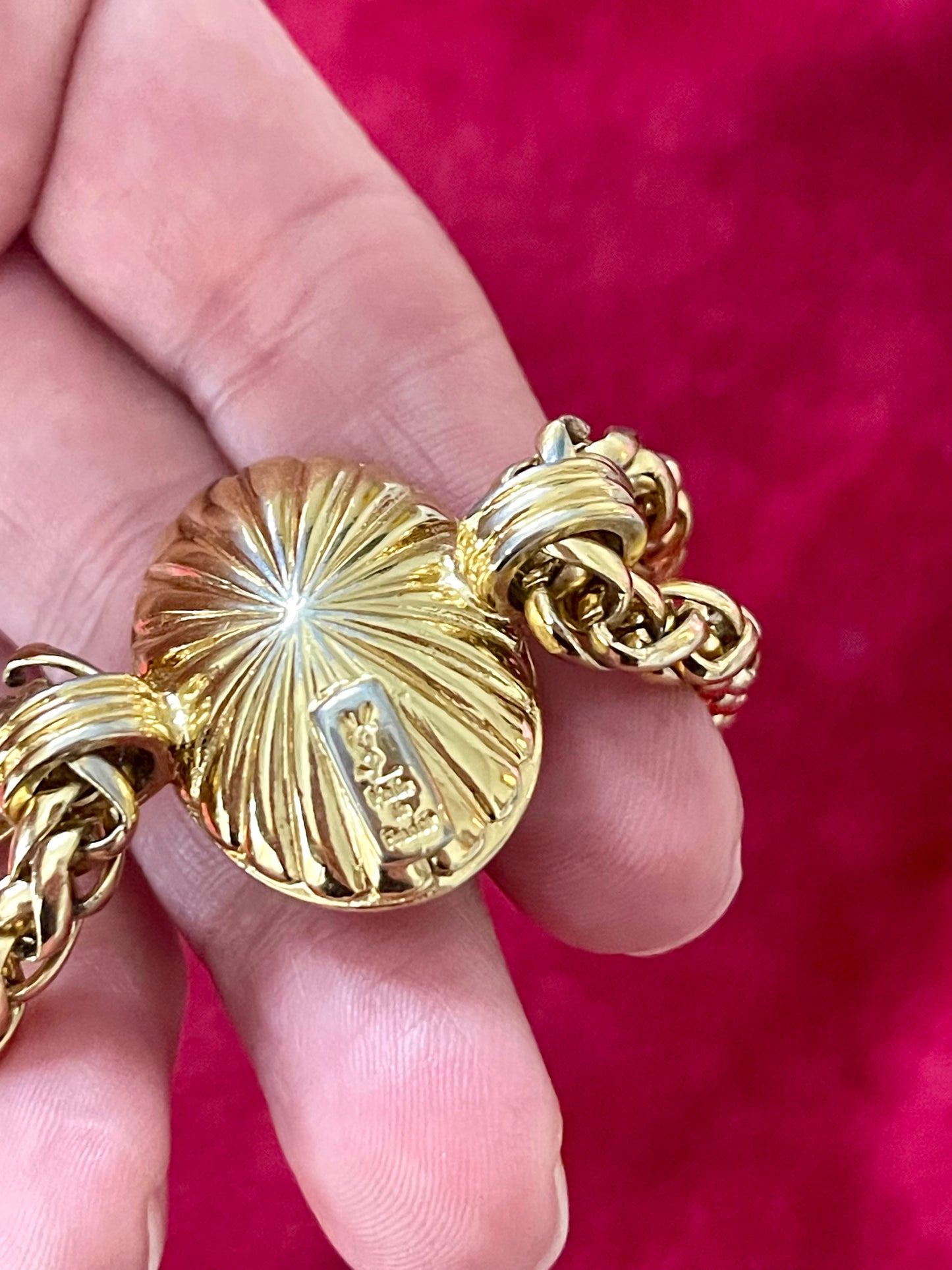 Gold YSL chain with a detailed signature held between fingers against a red background