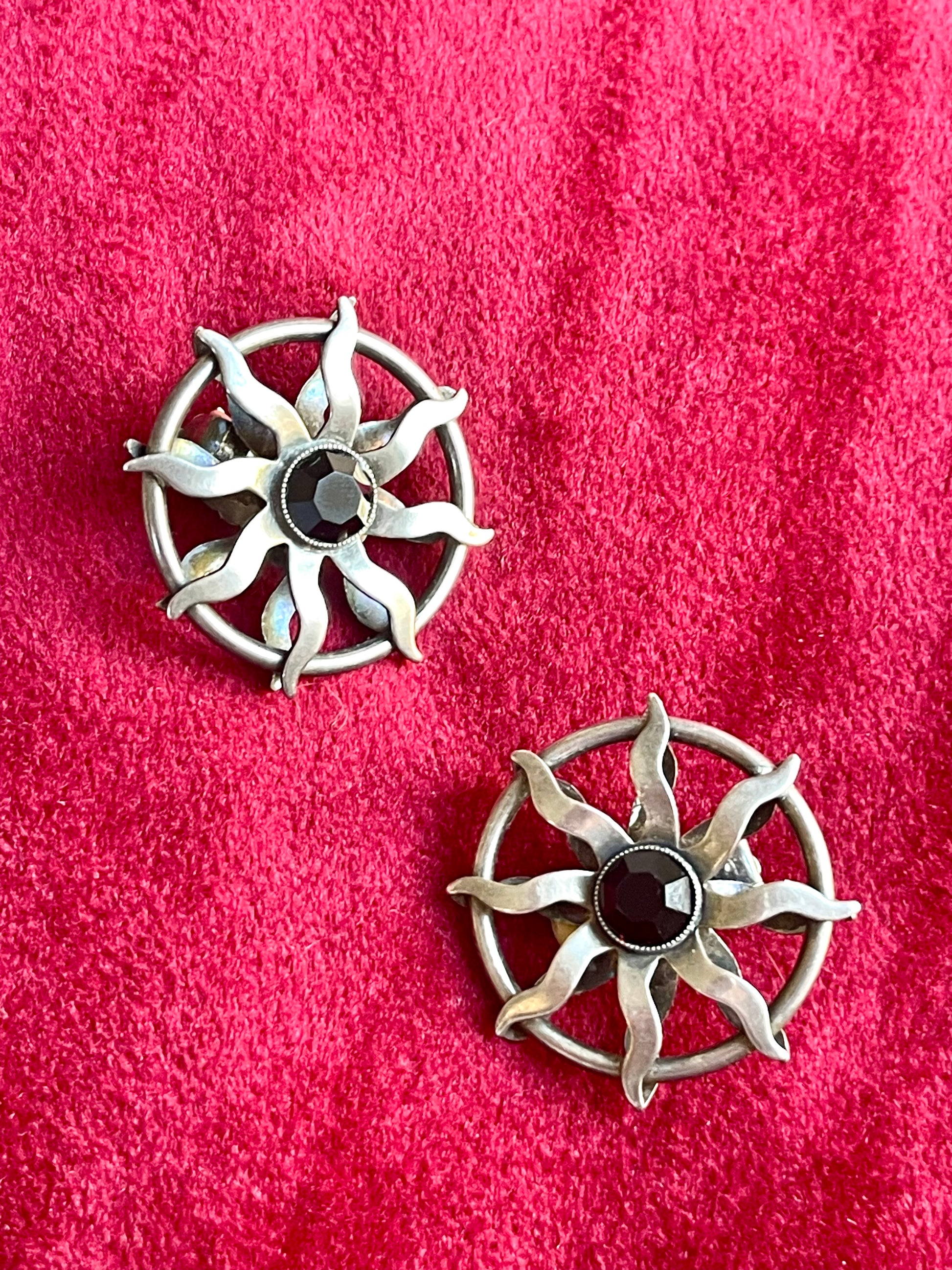 Vintage Paco Rabanne sun-design earrings in silver tone with black faceted stones, shown against a red fabric background.