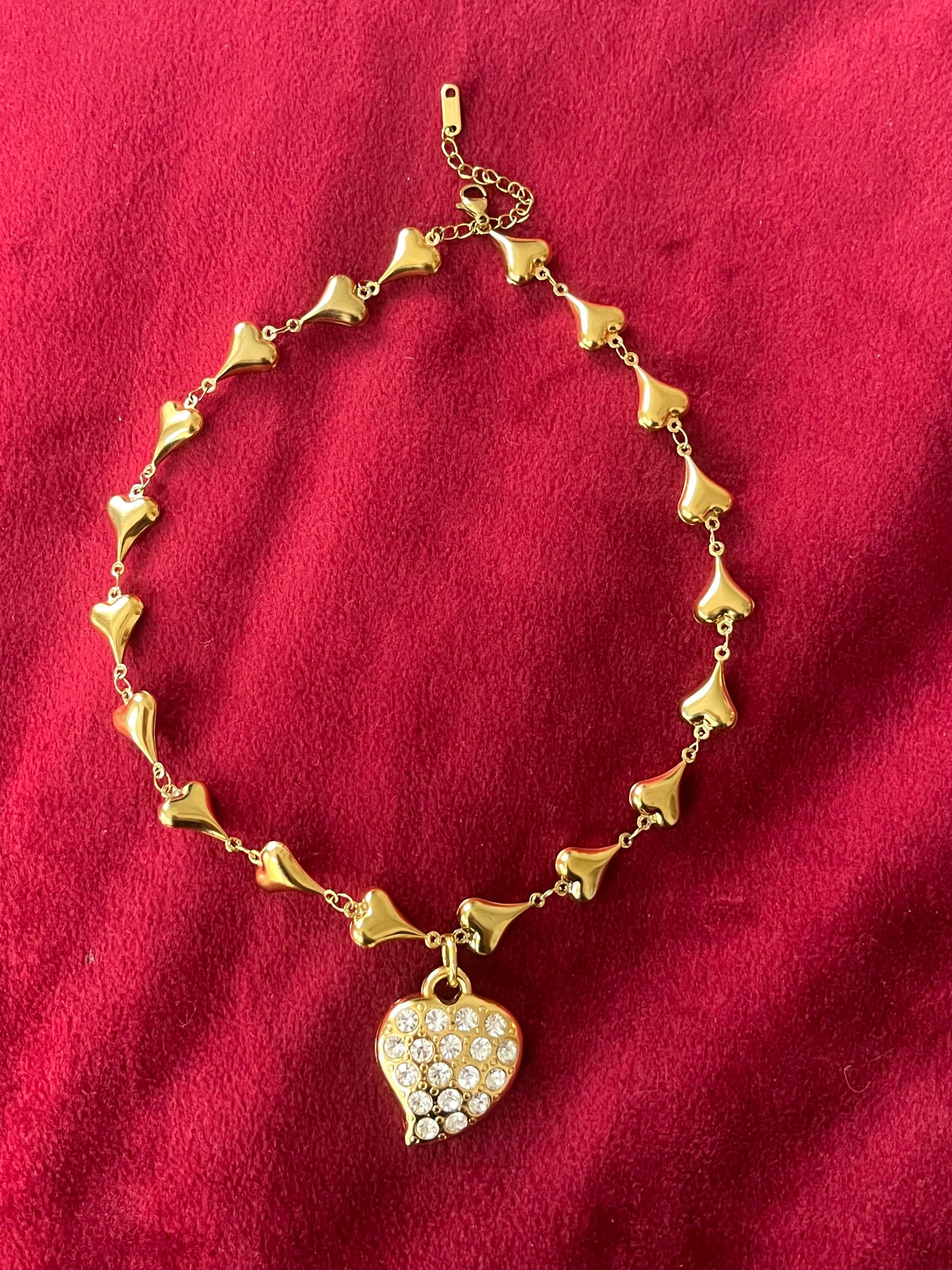 Full top view Vintage Yves Saint Laurent heart rhinestone pendant necklace with gold stainless steel chain on pink background