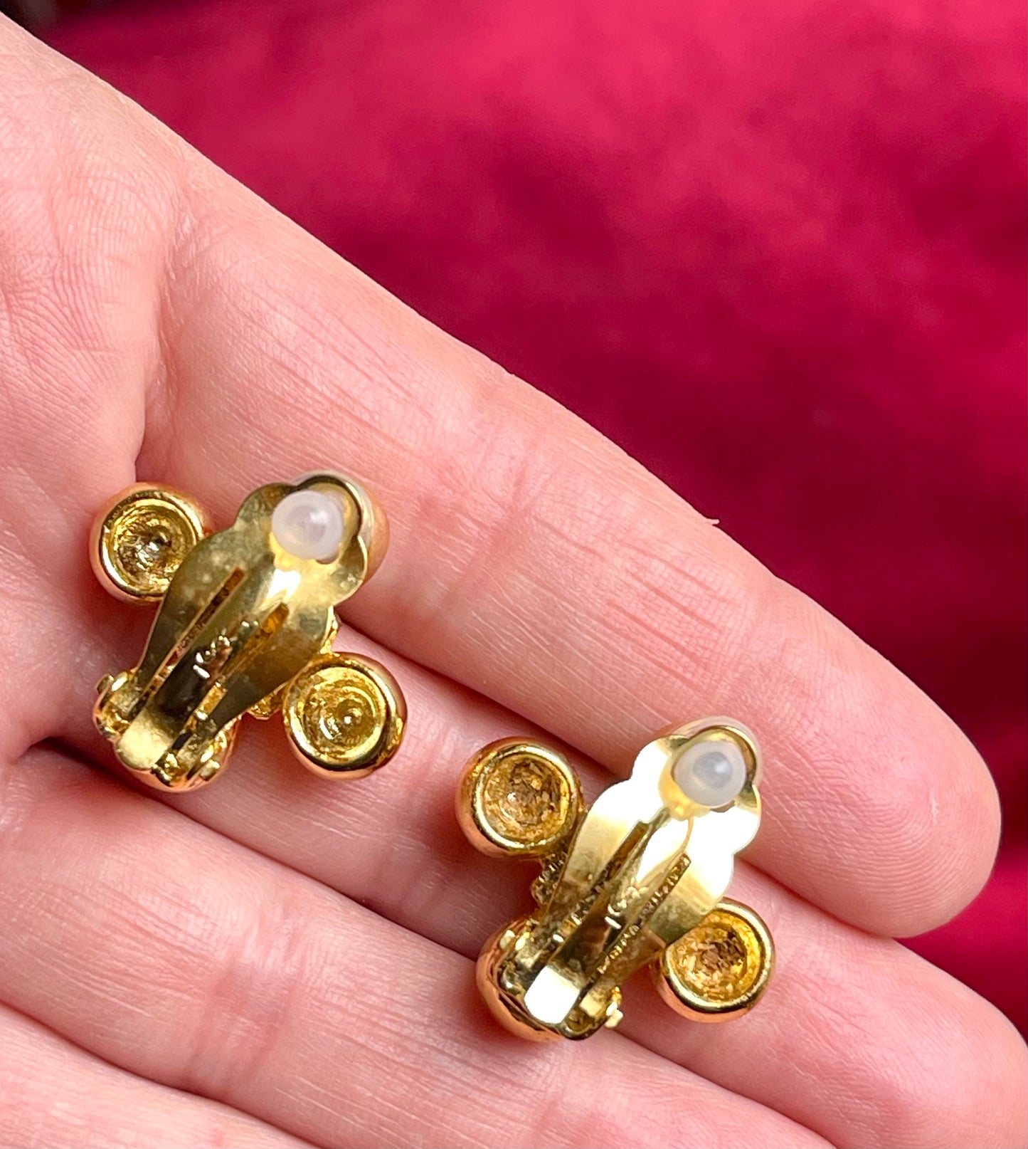 Close up back view Yves Saint Laurent vintage gold tone cross clip-on earrings from the 1980s held in hand, showing rounded gold domes and square-cut center stones