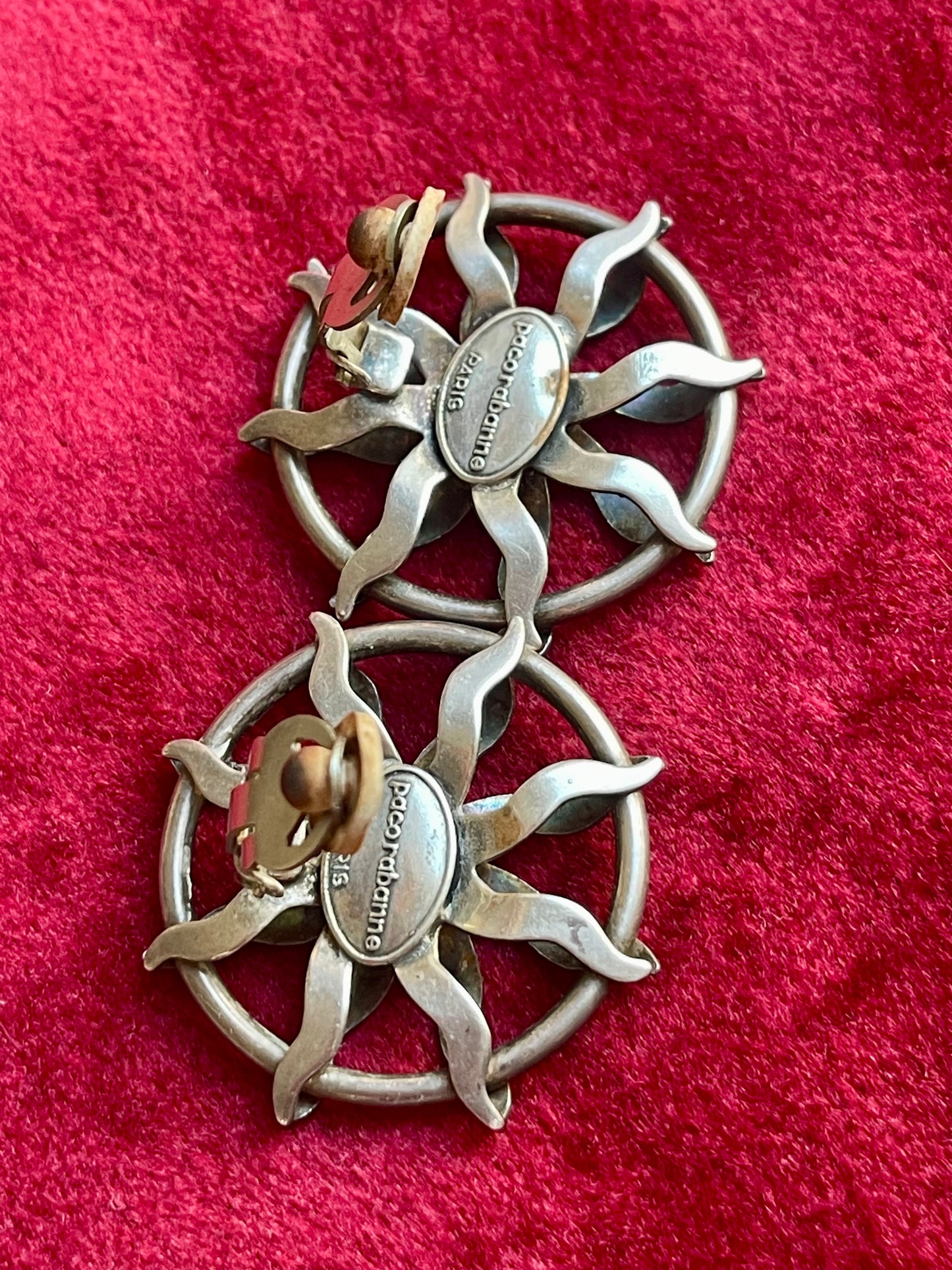 Showing hallmarks of Vintage Paco Rabanne sun-design earrings in silver tone with black faceted stones, shown against a red fabric background.
