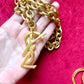 Displayed on hand Authentic YSL oversized gold logo bag charm pendant repurposed into a long chain necklace, close-up detail vintage Yves Saint Laurent 