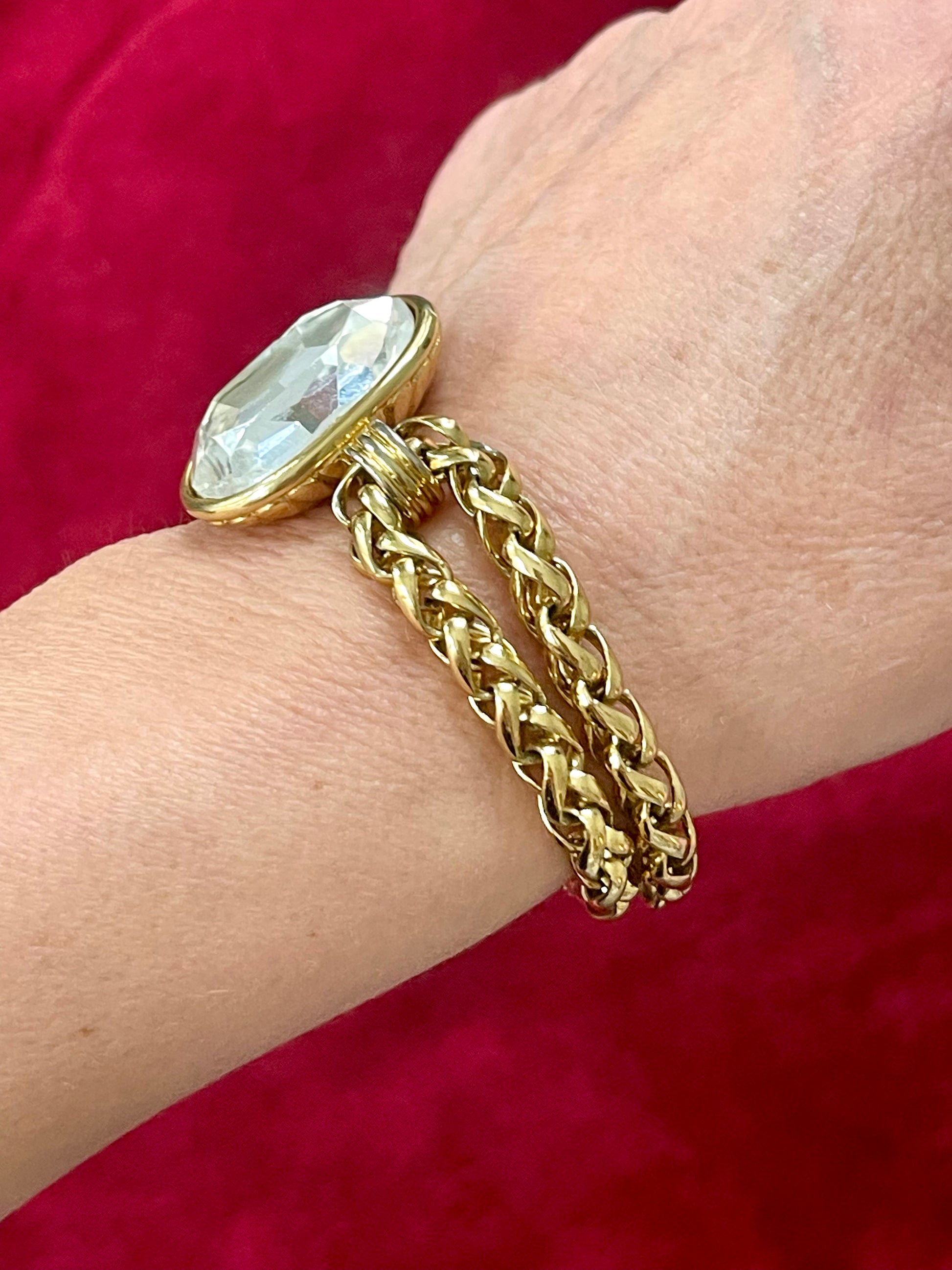 Gold bracelet  YSL with a large crystal on side wrist against a red background