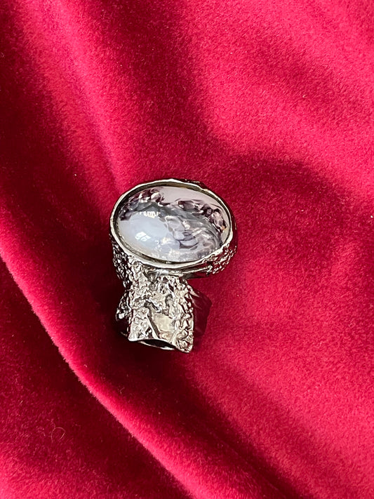 Flat lay of the Yves Saint Laurent Arty ring on a white background, focusing on the centerpiece cabochon and artistic metalwork on red velvet background 