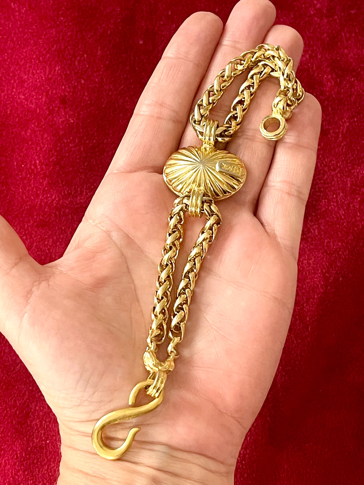 Back side view of Vintage Yves Saint Laurent crystal chain bracelet signed YSL Made in France placed on hand with a red background 