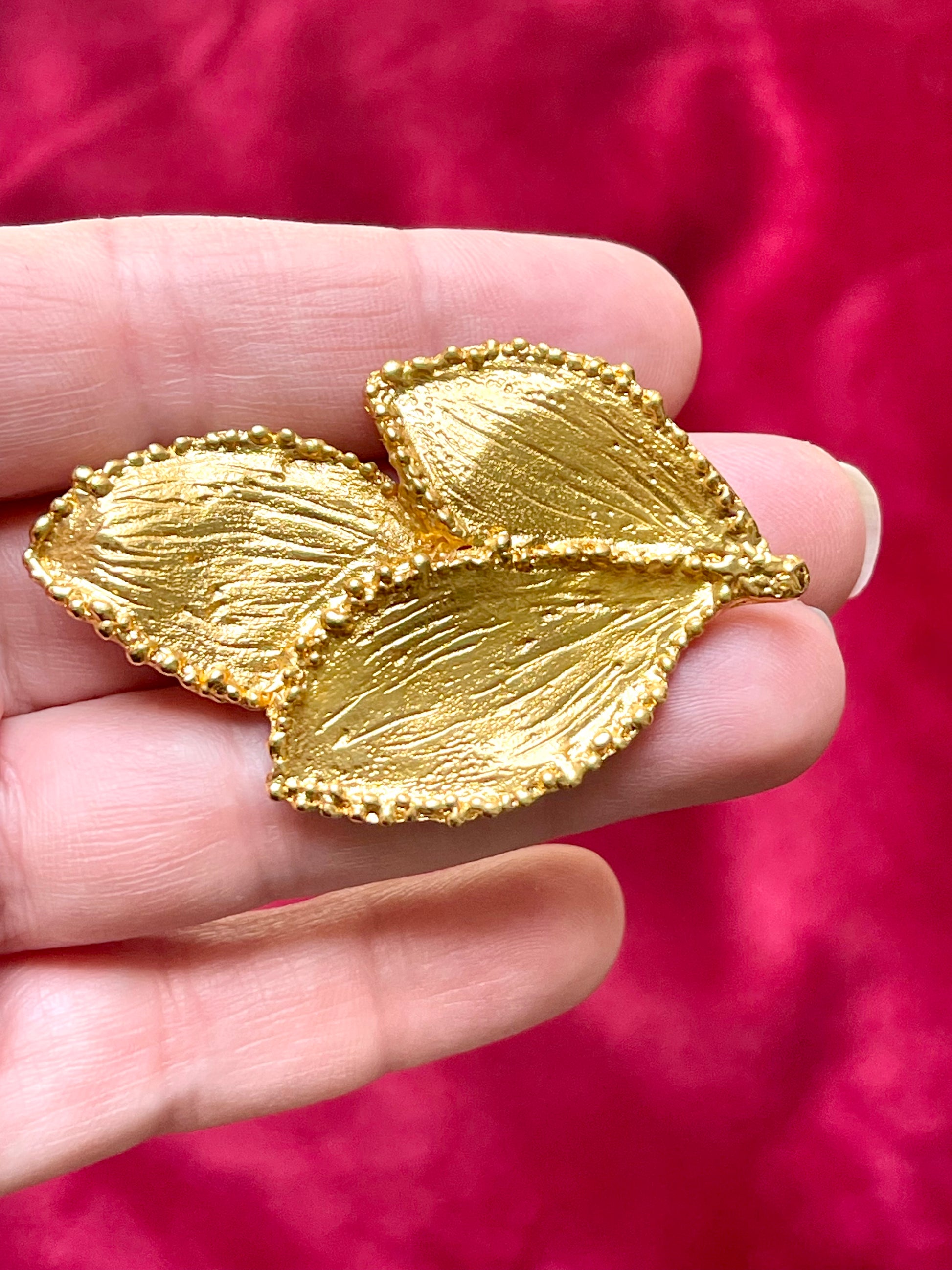 On hand close up Vintage Yves Saint Laurent 80s 90s gold tone leaf brooch excellent condition on red velvet background 