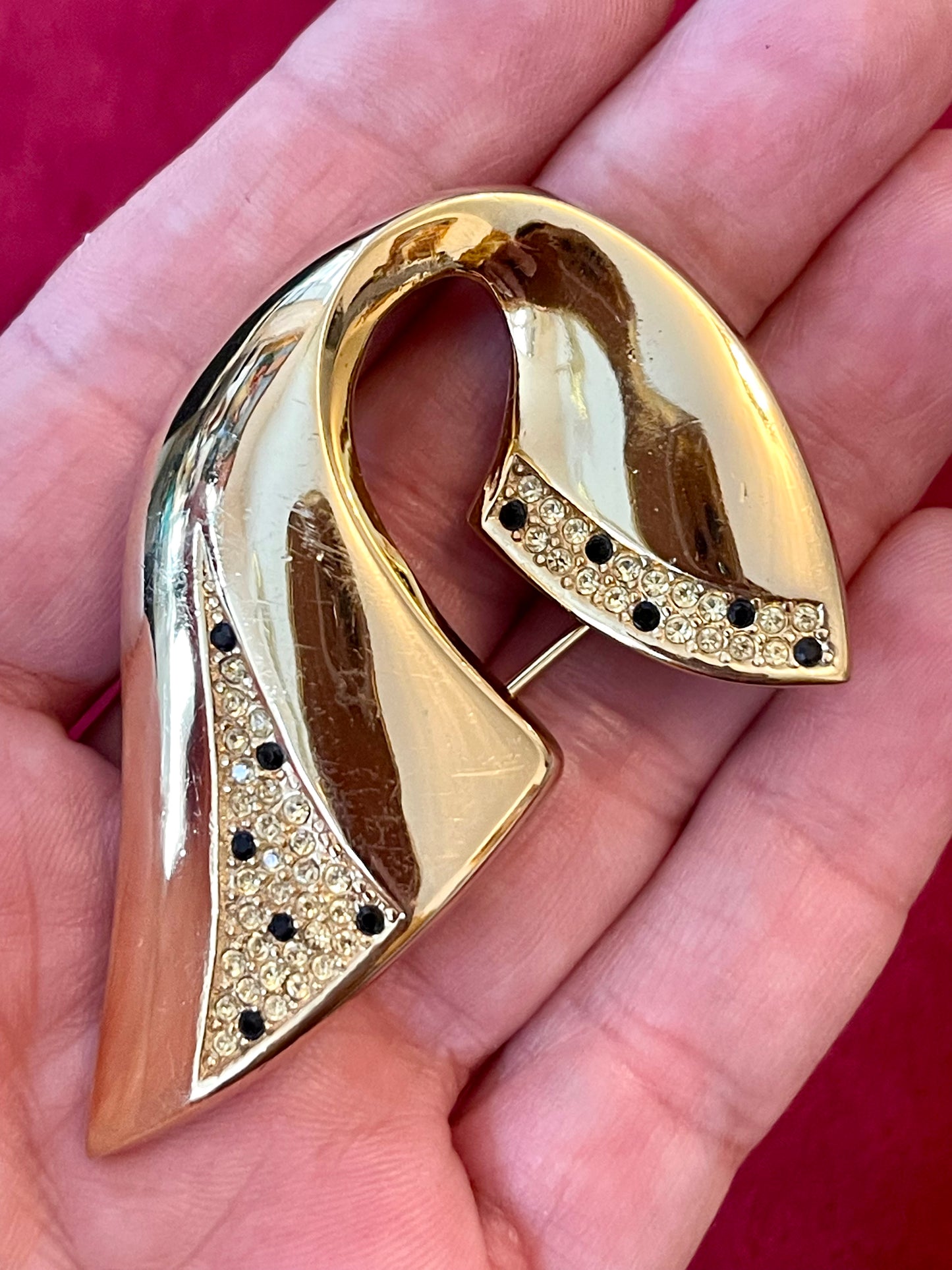 Vintage Christian Dior gold-tone sculptural brooch decorated with black and clear rhinestones, displayed on hand against a red background