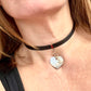 Person wearing a black leather Yves Saint Laurent choker necklace with a heart-shaped pendant and logo charm YSL