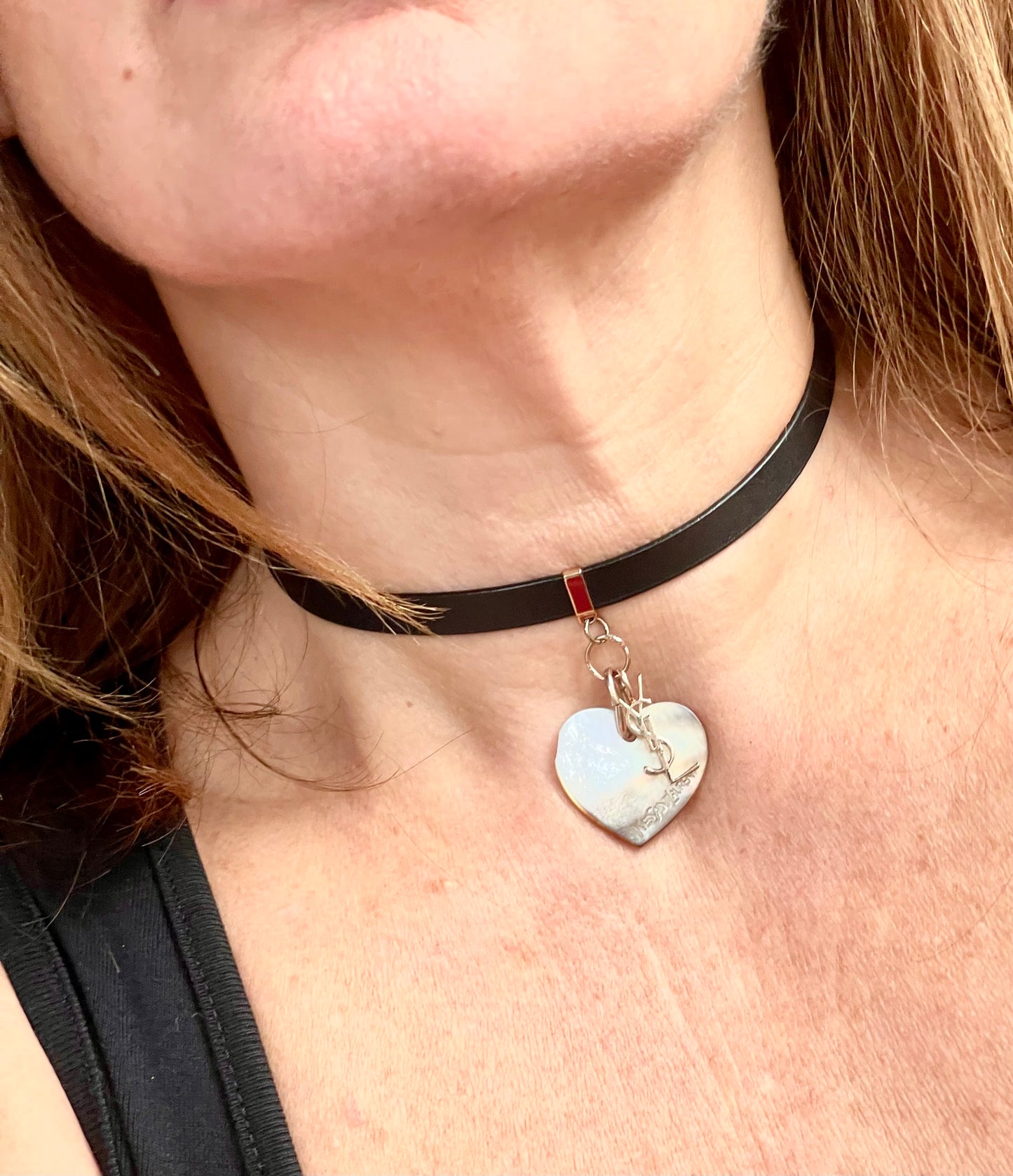 Person wearing a black leather Yves Saint Laurent choker necklace with a heart-shaped pendant and logo charm YSL