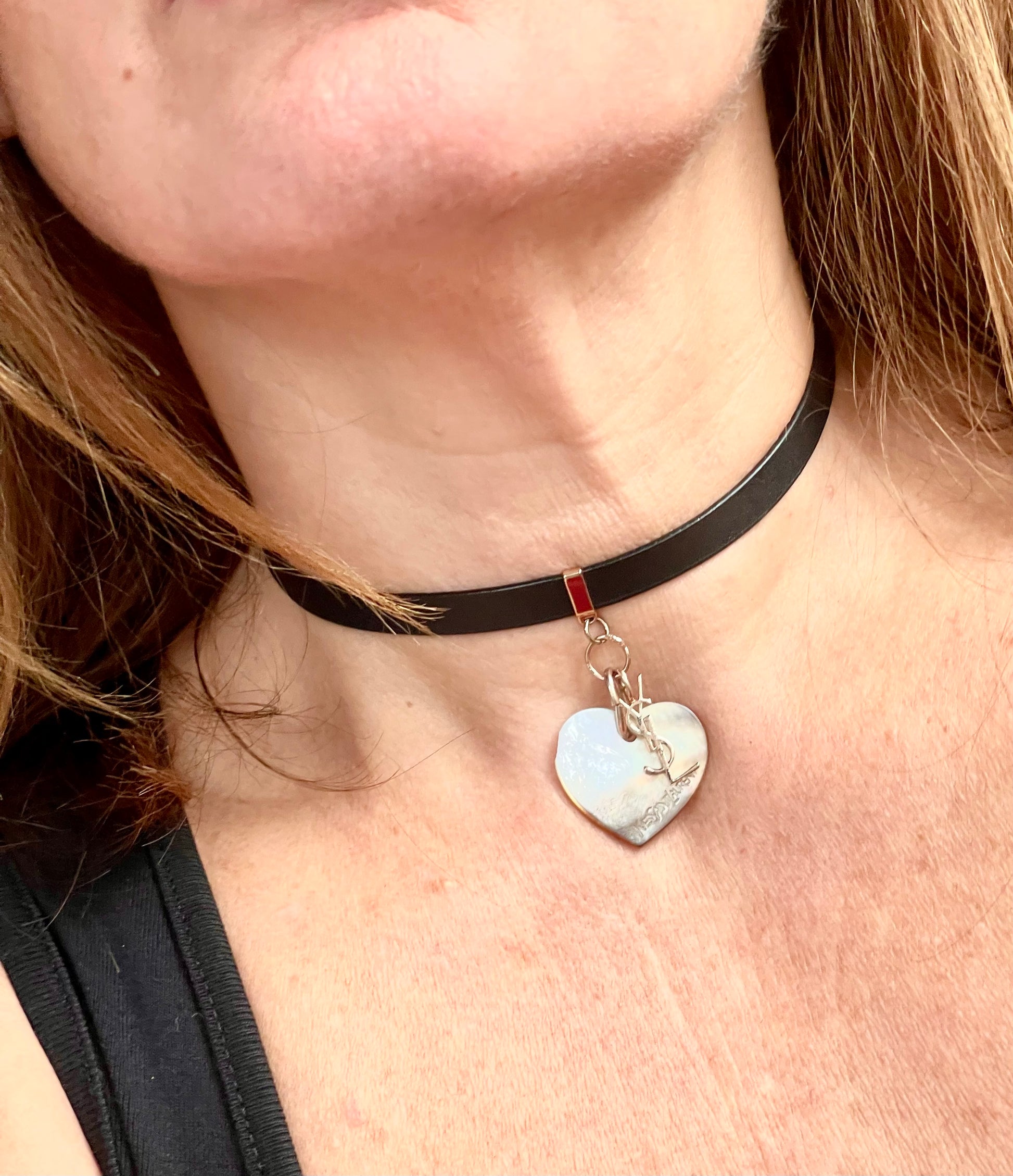 Person wearing a black leather Yves Saint Laurent choker necklace with a heart-shaped pendant and logo charm YSL