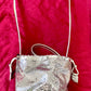Full view of Paco Rabanne silver shoulder/wrist bag with long  strap shown, on red velvet fabric background.