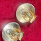 Vintage gold-tone shell-shaped back side of Yves Saint Laurent earrings displayed on red fabric with textured surface in excellent condition.