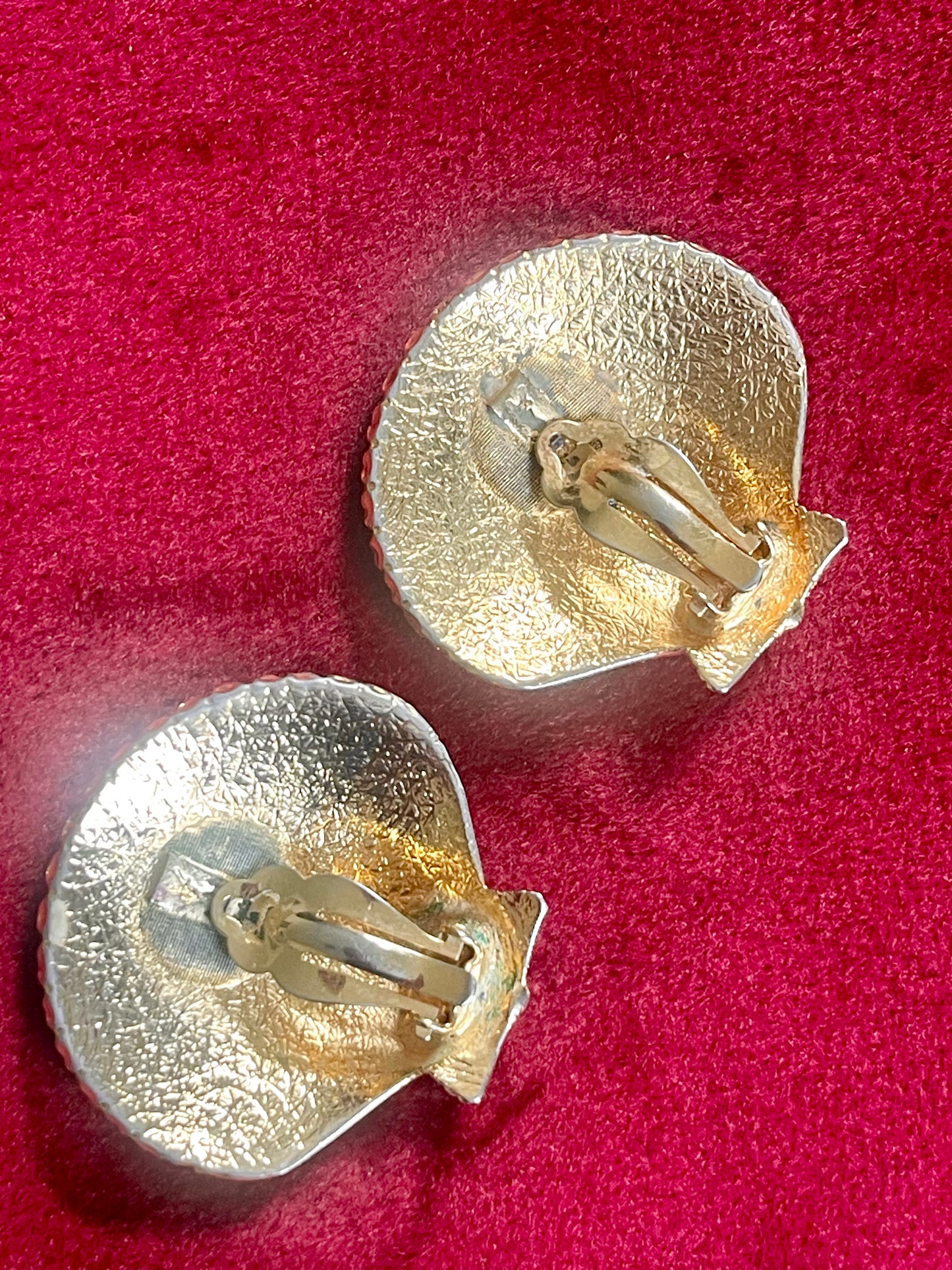 Vintage gold-tone shell-shaped back side of Yves Saint Laurent earrings displayed on red fabric with textured surface in excellent condition.
