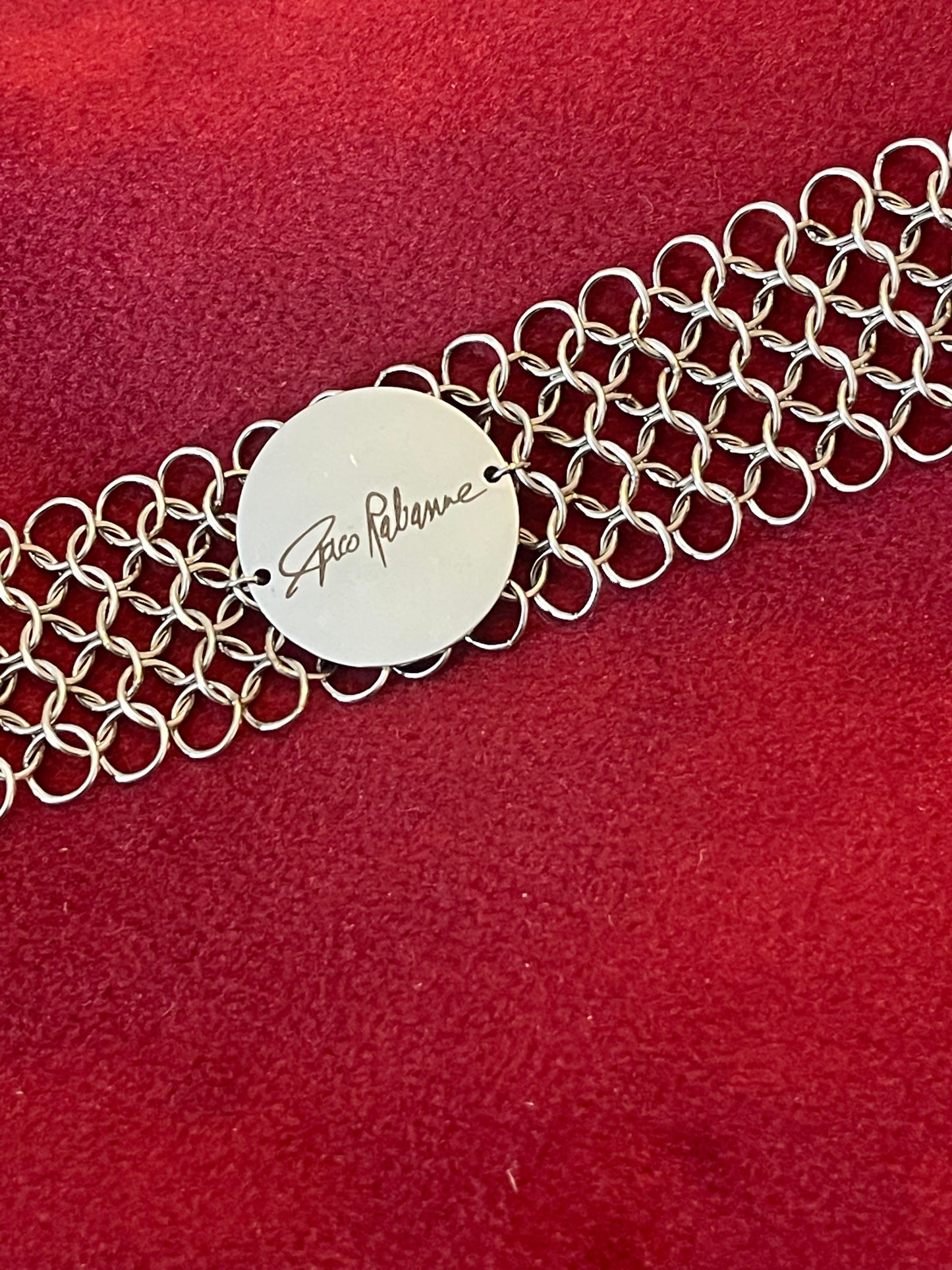 Signed Paco Rabanne mesh bracelet medallion detail On red background 