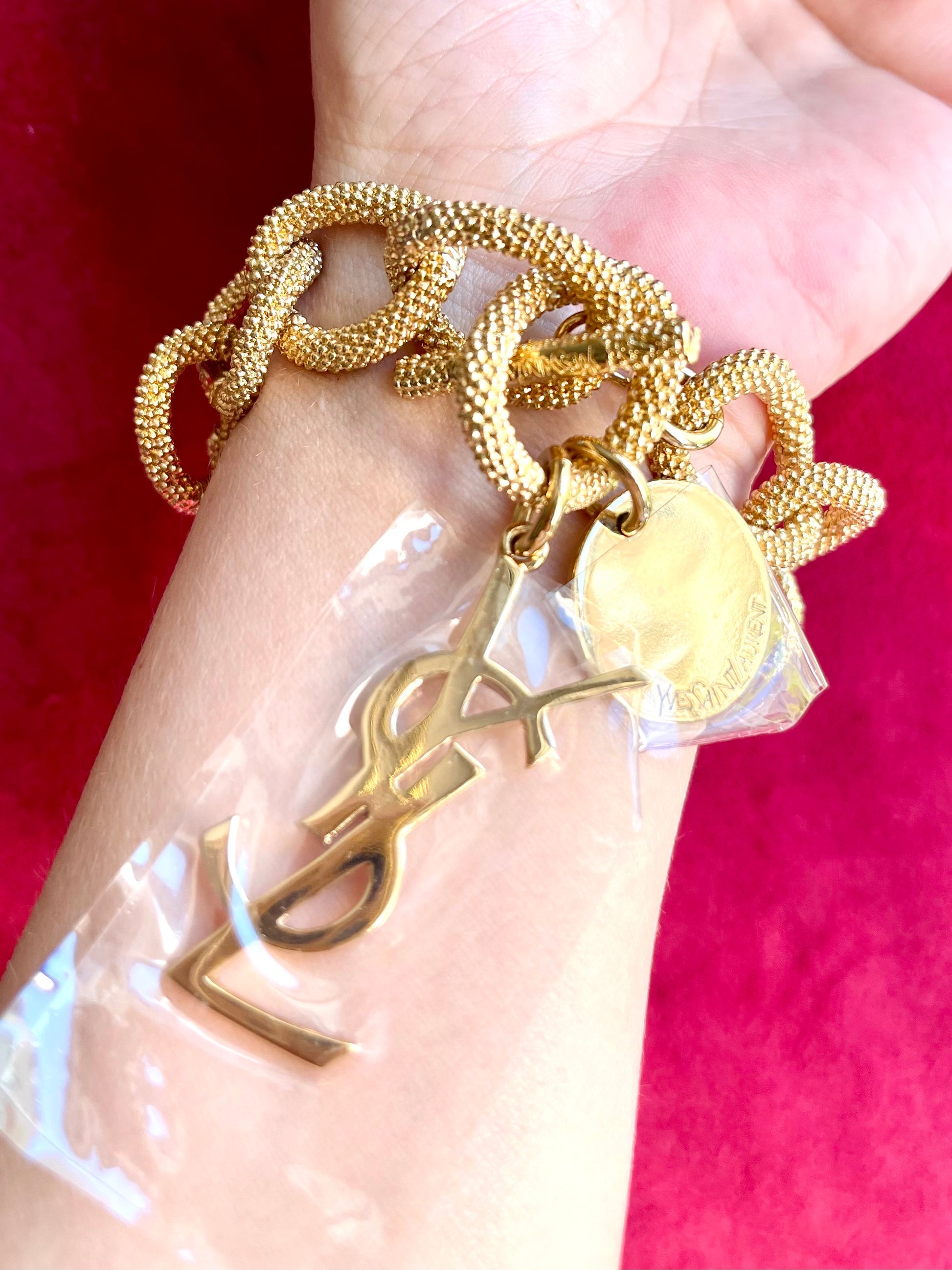 Close up Gold-tone vintage YSL chain bracelet worn on wrist with YSL logo charm and medallion