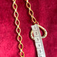 Gold chain with a measuring tape heart pendant on a red background