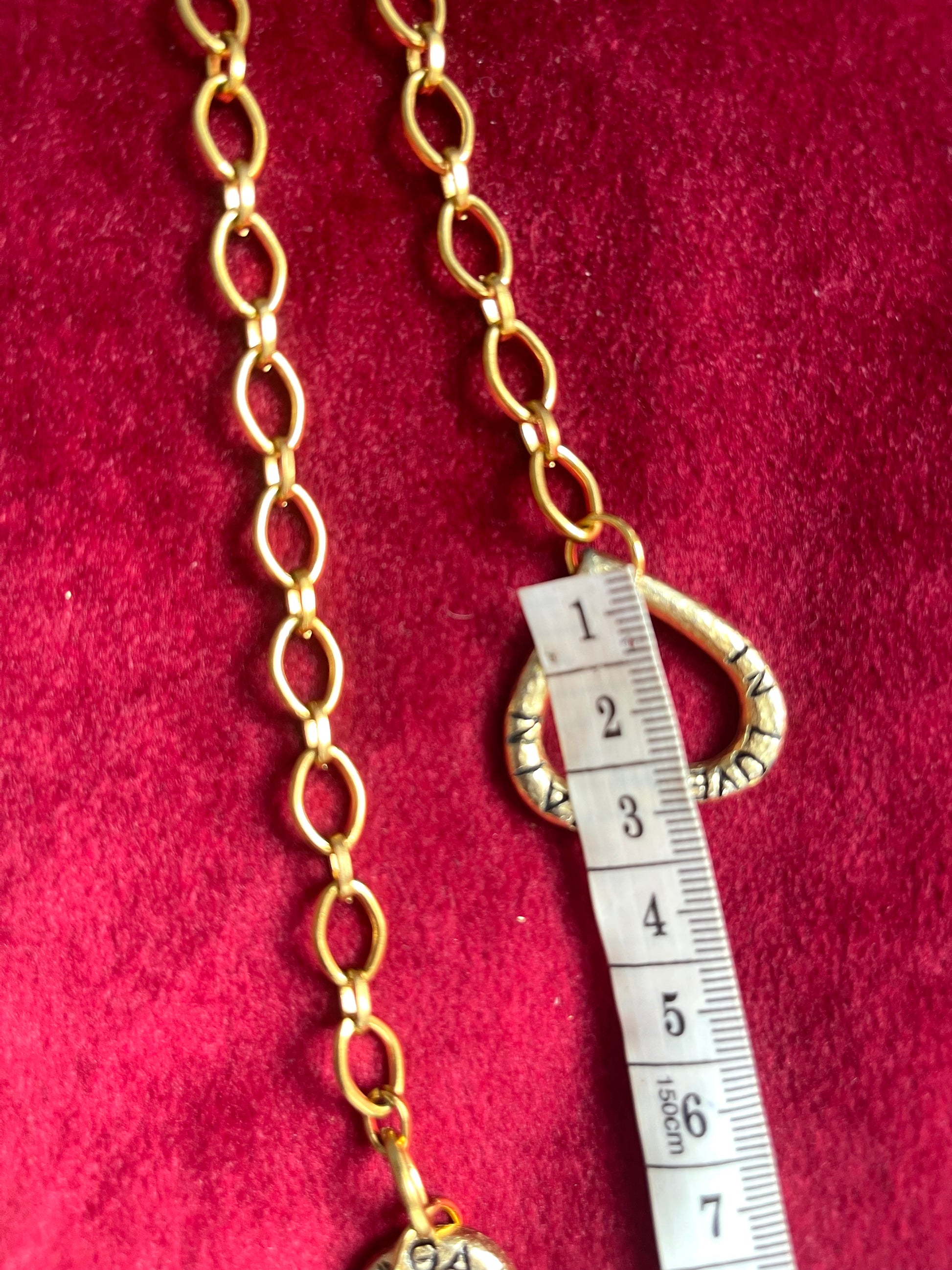 Gold chain with a measuring tape heart pendant on a red background