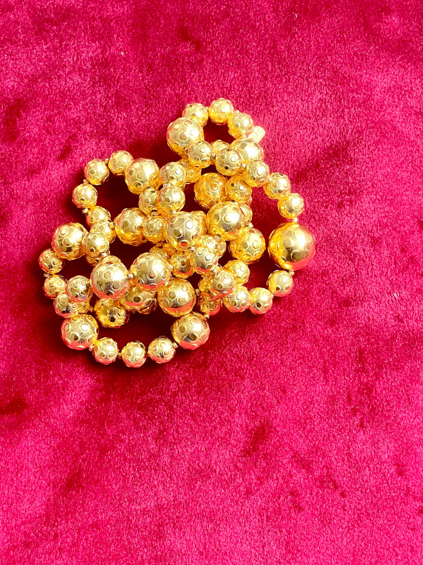 Vintage Yves Saint Laurent gold beaded necklace with textured graduated beads displayed on red velvet background.