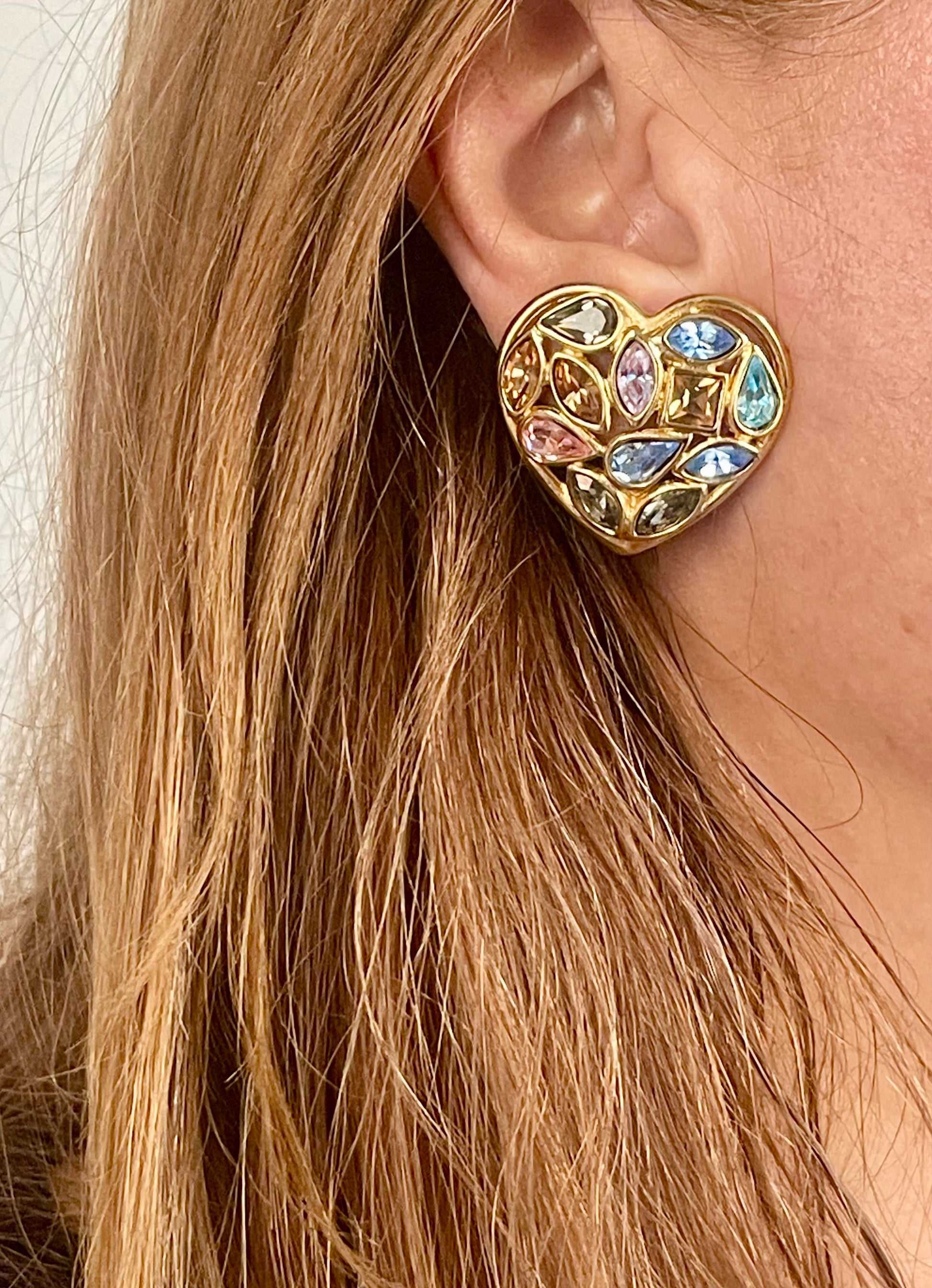 Close up of a person wearing   gold-tone vintage Yves Saint Laurent heart-shaped clip-on earrings decorated with multi-colored crystals vintage 80s