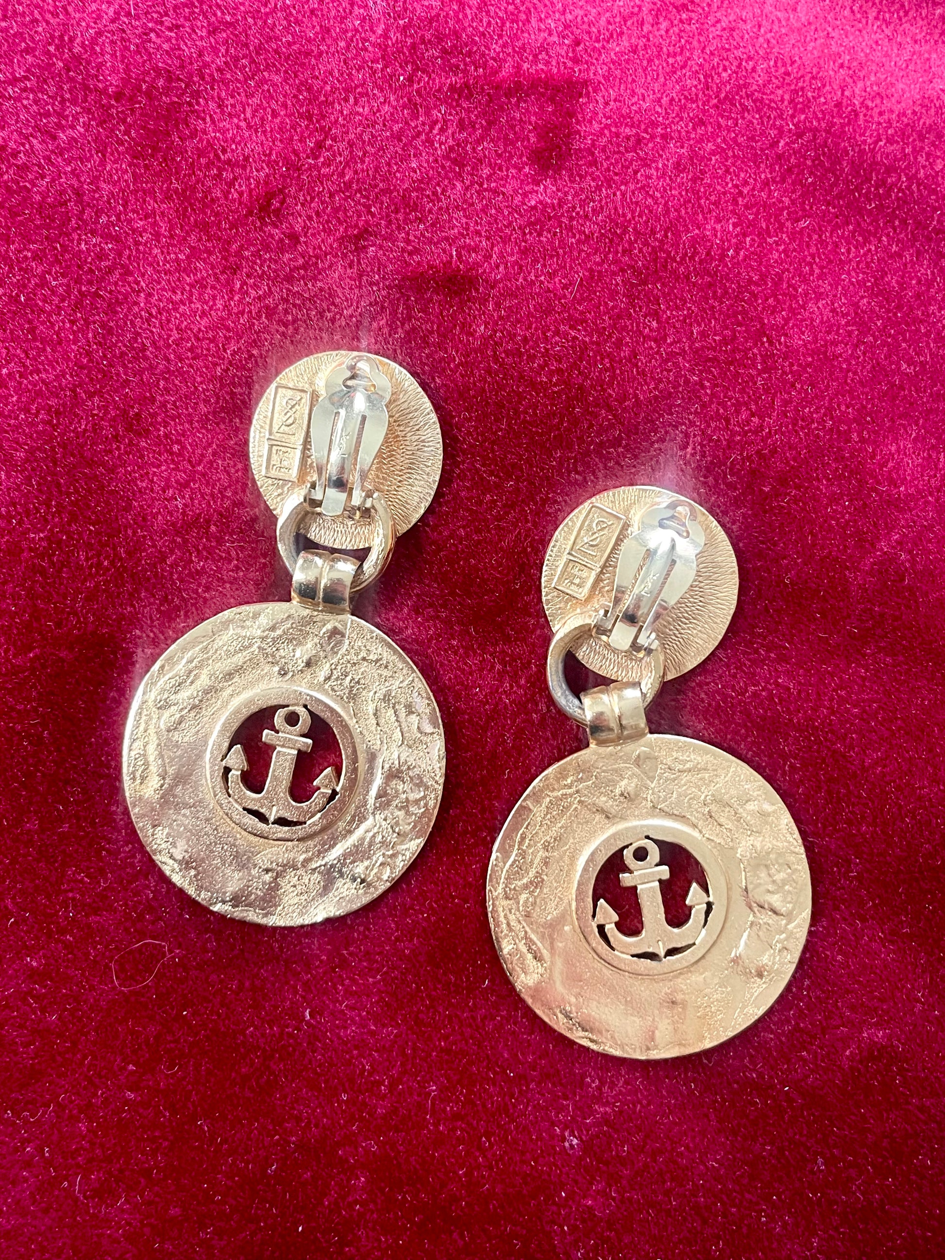 Back of Yves Saint Laurent gold-tone anchor earrings with engraved signatures red background 