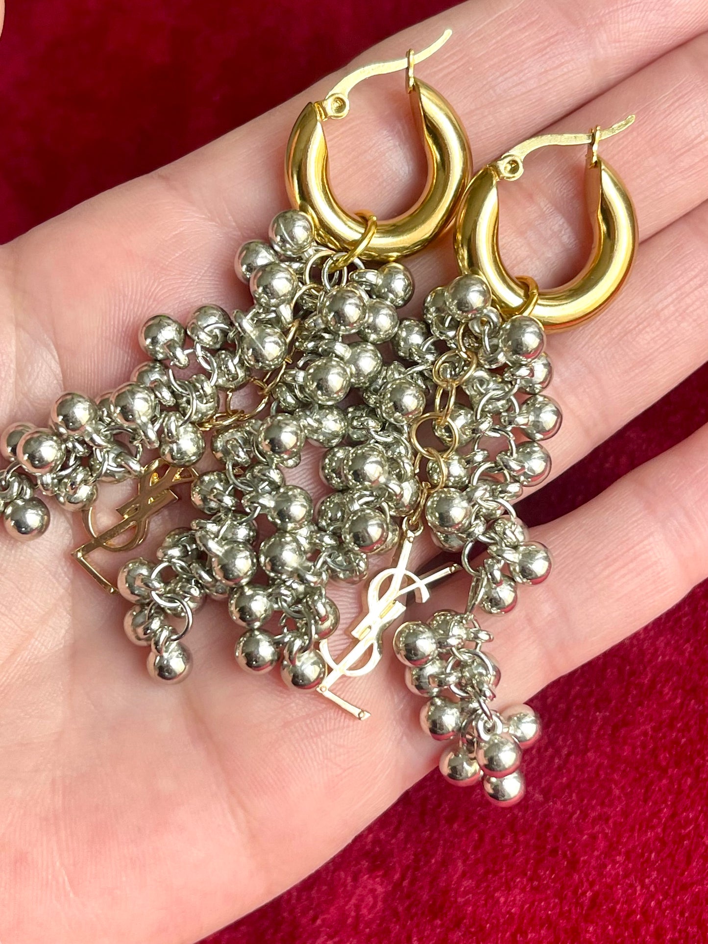 On hand close up of Gold and silver earrings with pearl-like beads and YSL Yves Saint Laurent charms