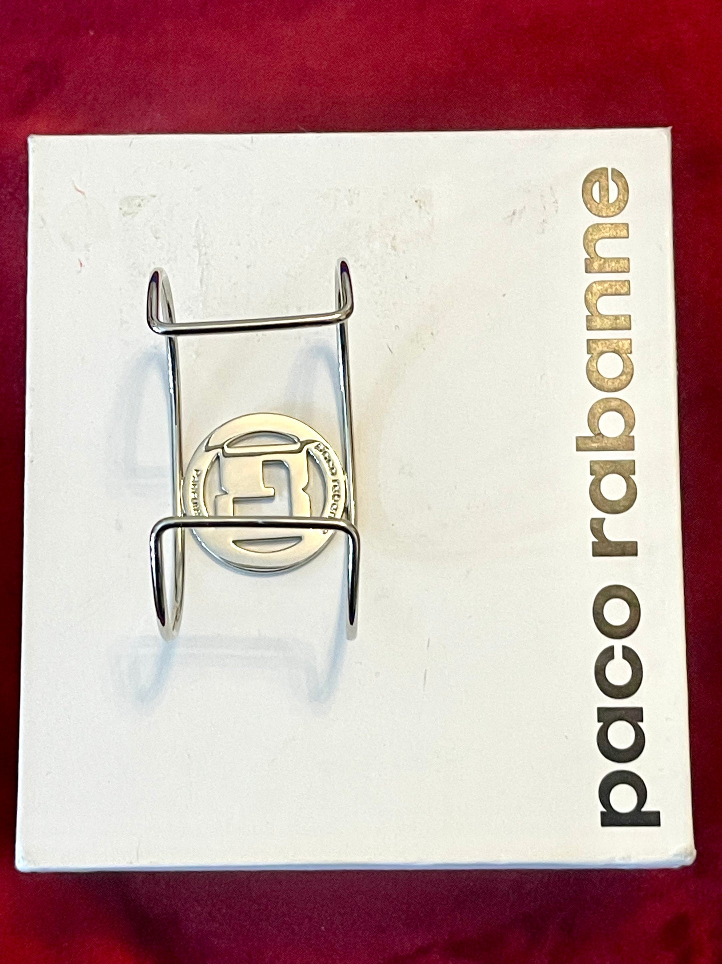 Back view of signed Paco Rabanne Parfums cuff bracelet on white and red background 
