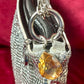 Close on the yellow gemstone charm of repurposed Paco Rabanne silver mesh bag on a red background