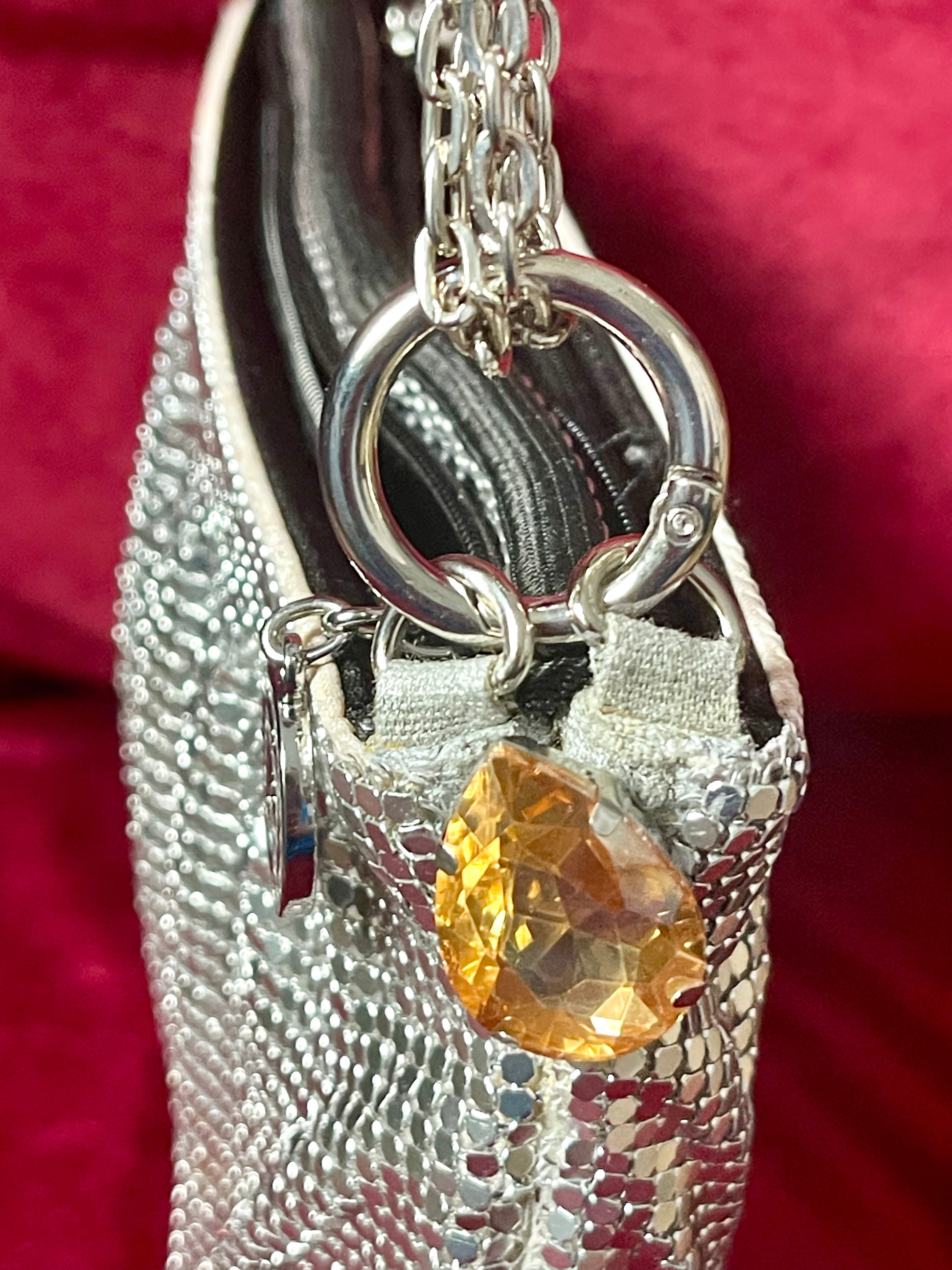 Close on the yellow gemstone charm of repurposed Paco Rabanne silver mesh bag on a red background