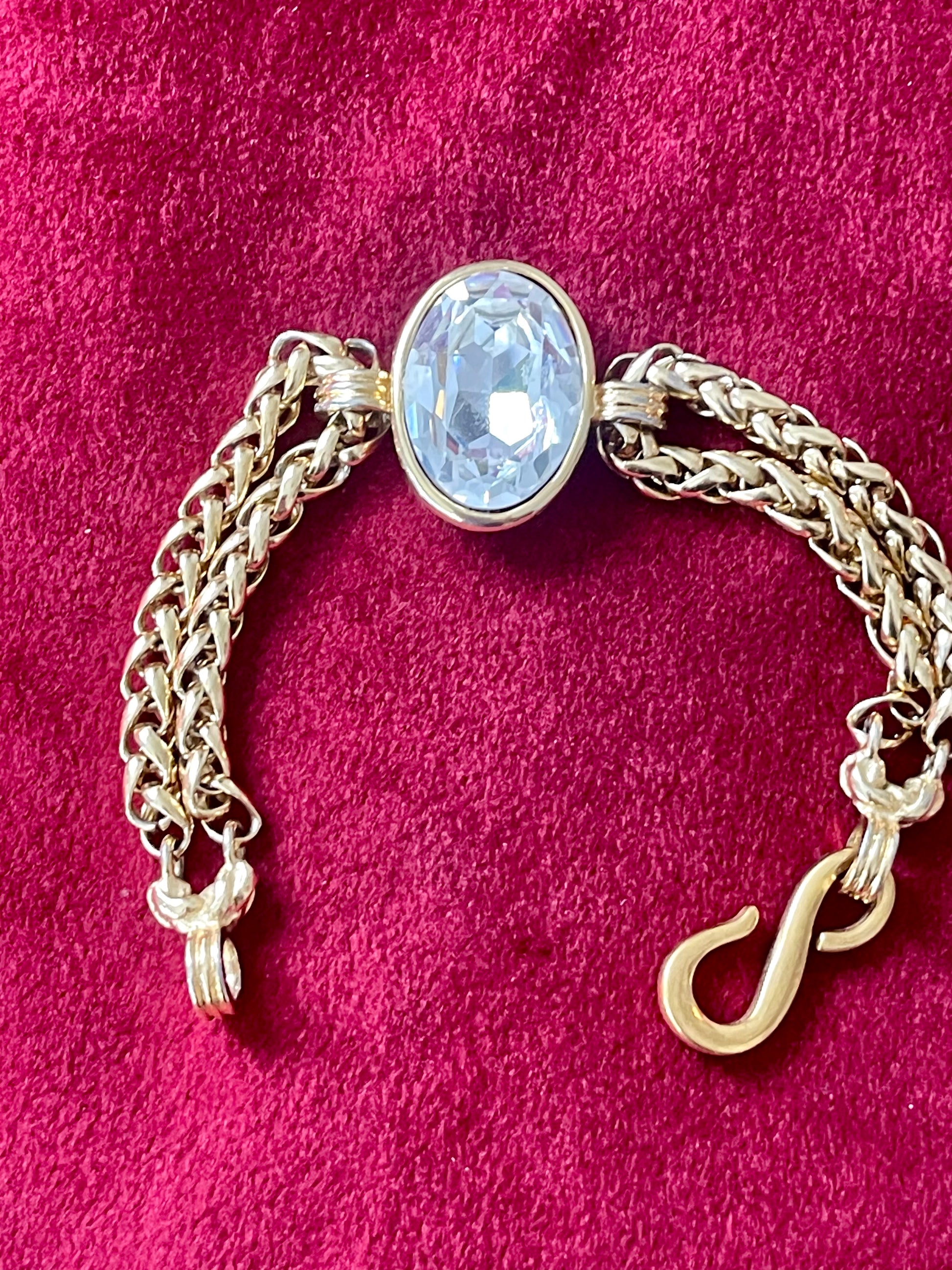 YSL gold tone statement bracelet with oval crystal centerpiece On a red background 