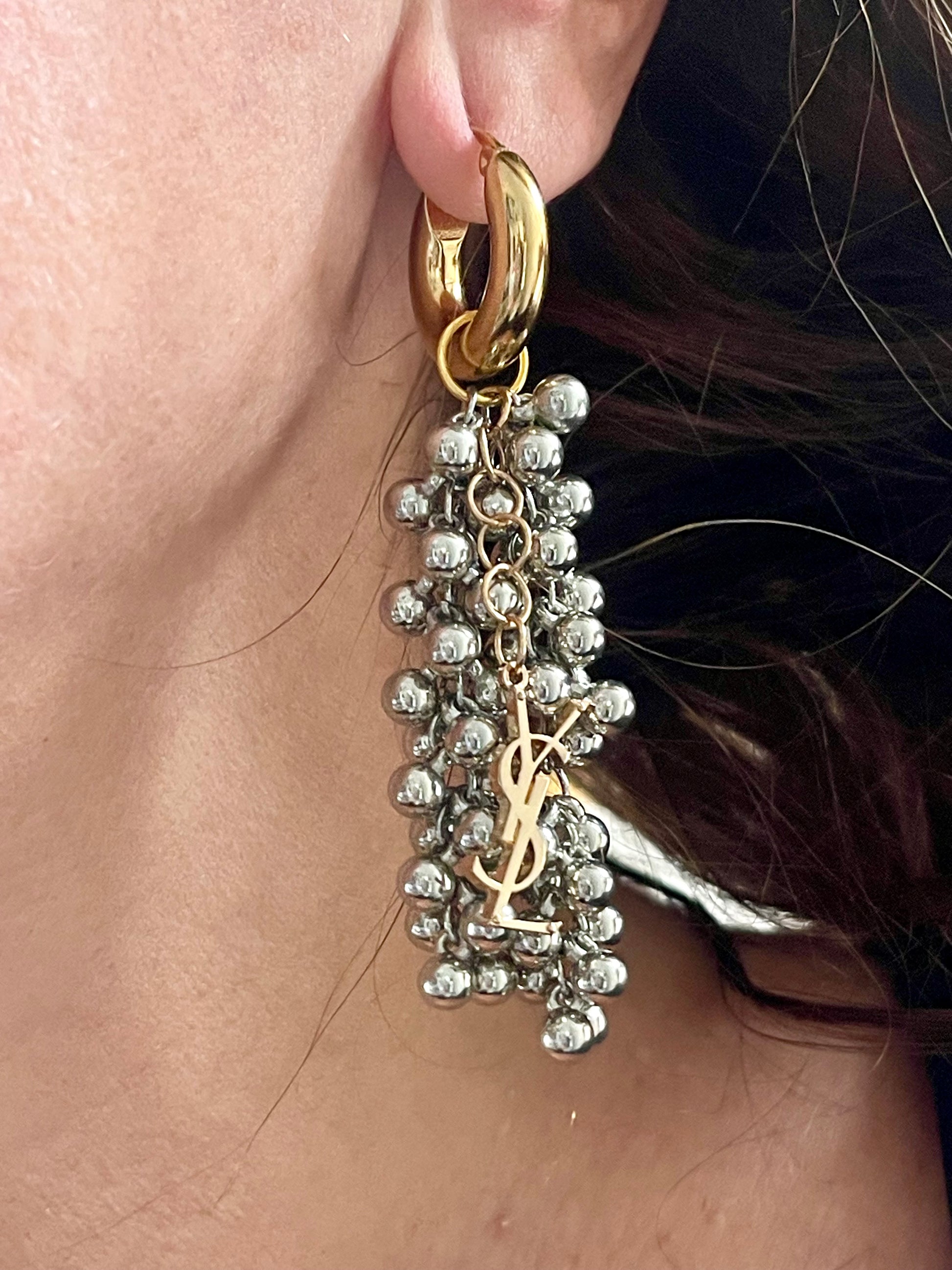 Gold and silver earring with dangling beads and YSL charm worn by a person