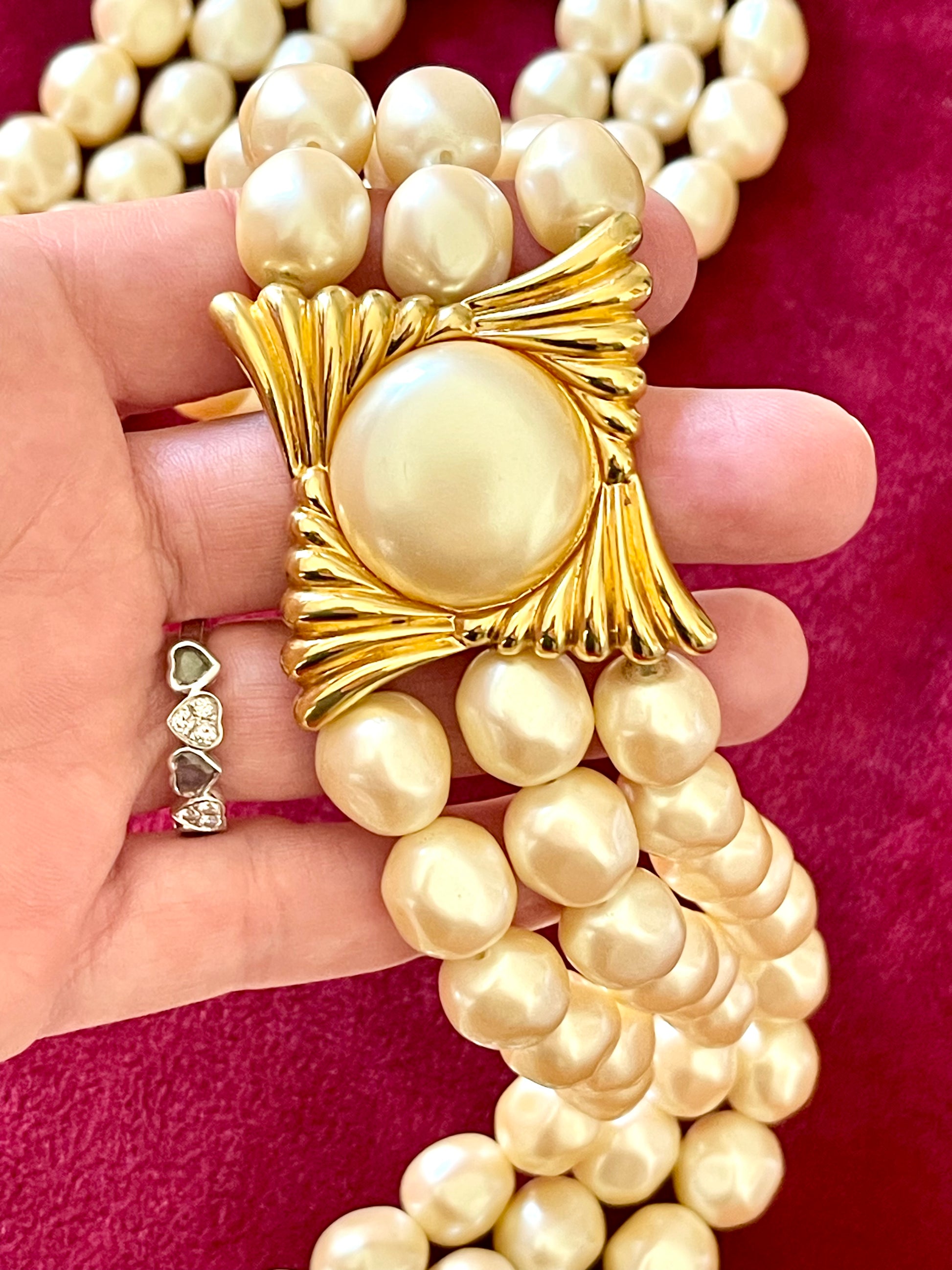 Close-up of gold-tone sculptural clasp with domed faux pearl on a vintage YSL pearl necklace, held in hand to show detail and hallmark