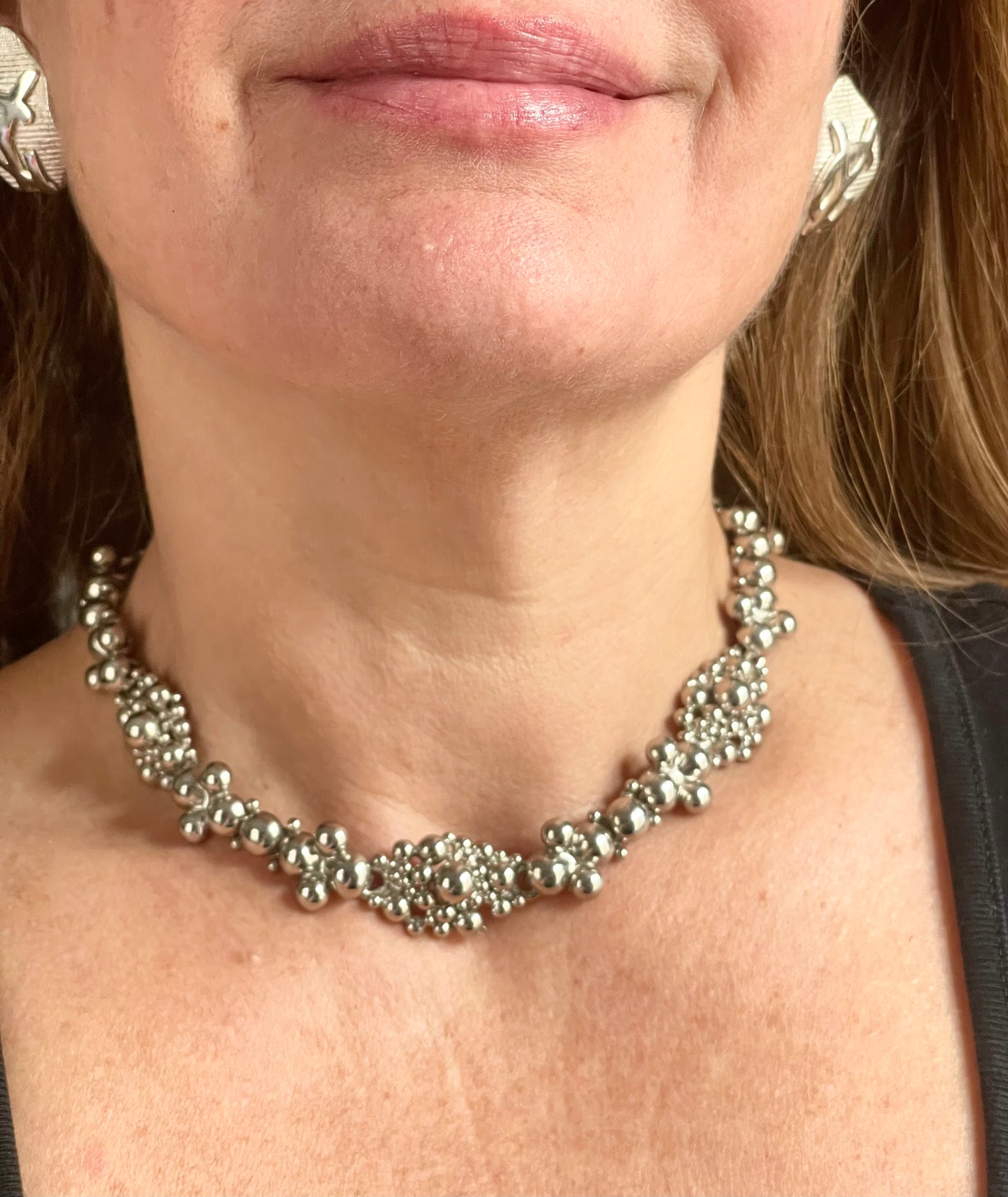 Close-up of a model wearing a vintage Yves Saint Laurent silver necklace with hexagonal YSL Monogram earrings.
