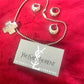 Vintage YSL silver jewelry set displayed on red fabric: silver earrings, cross pendant necklace on beaded chain, ring and YSL guarantee card