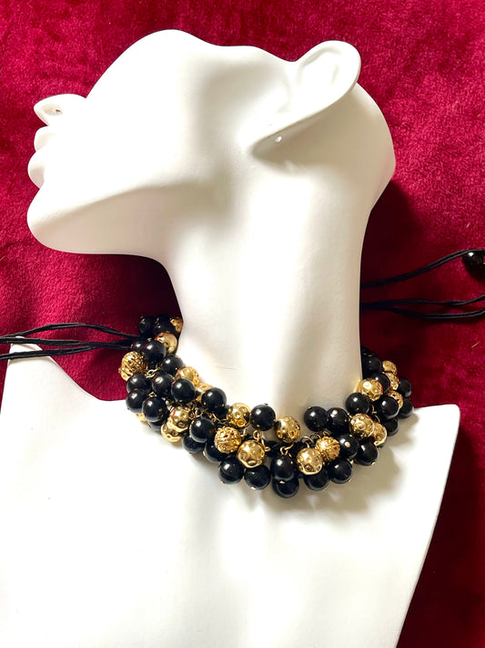 Vintage Yves Saint Laurent beaded necklace with black and gold beads, woven into braided black cotton cords, displayed on a red velvet background and white model 