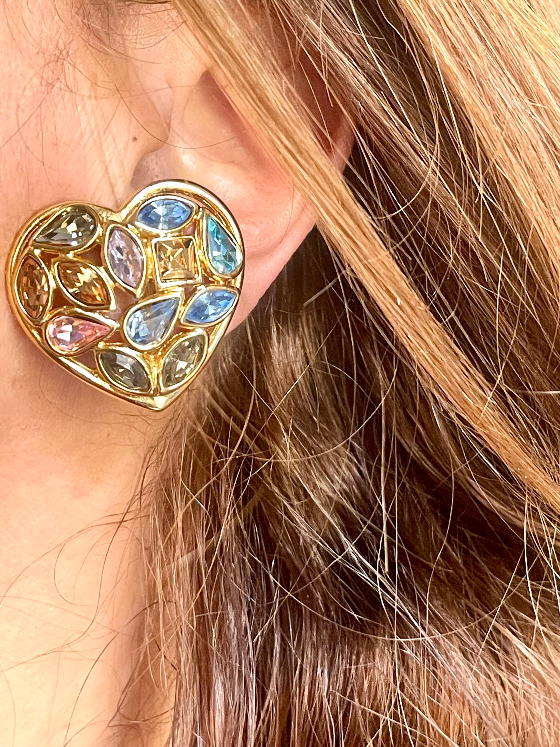 Close up of a person wearing   gold-tone vintage Yves Saint Laurent heart-shaped clip-on earrings decorated with multi-colored crystals vintage 80s