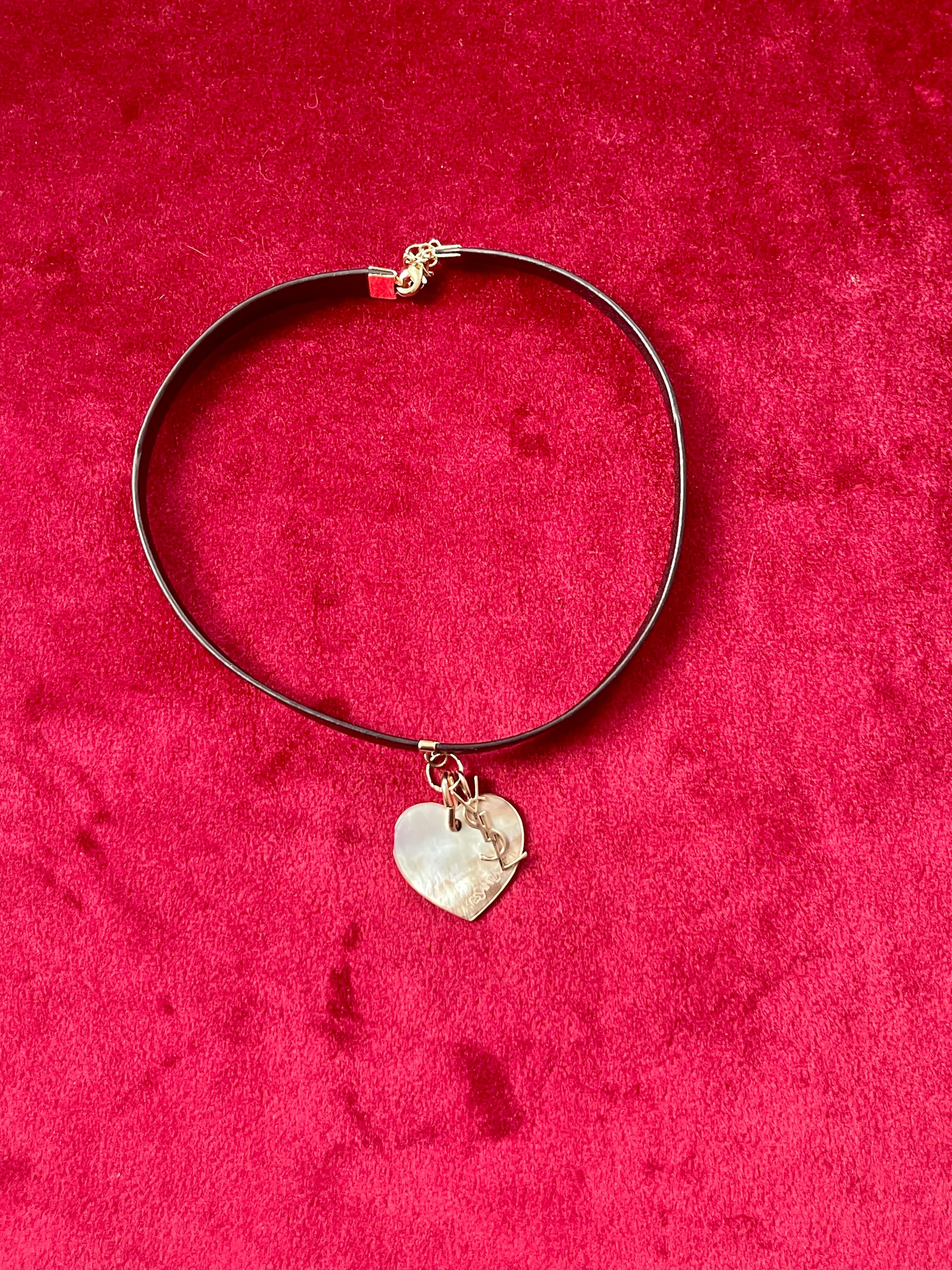 Black choker Yves Saint Laurent necklace with a heart-shaped pendant on a red textured background
