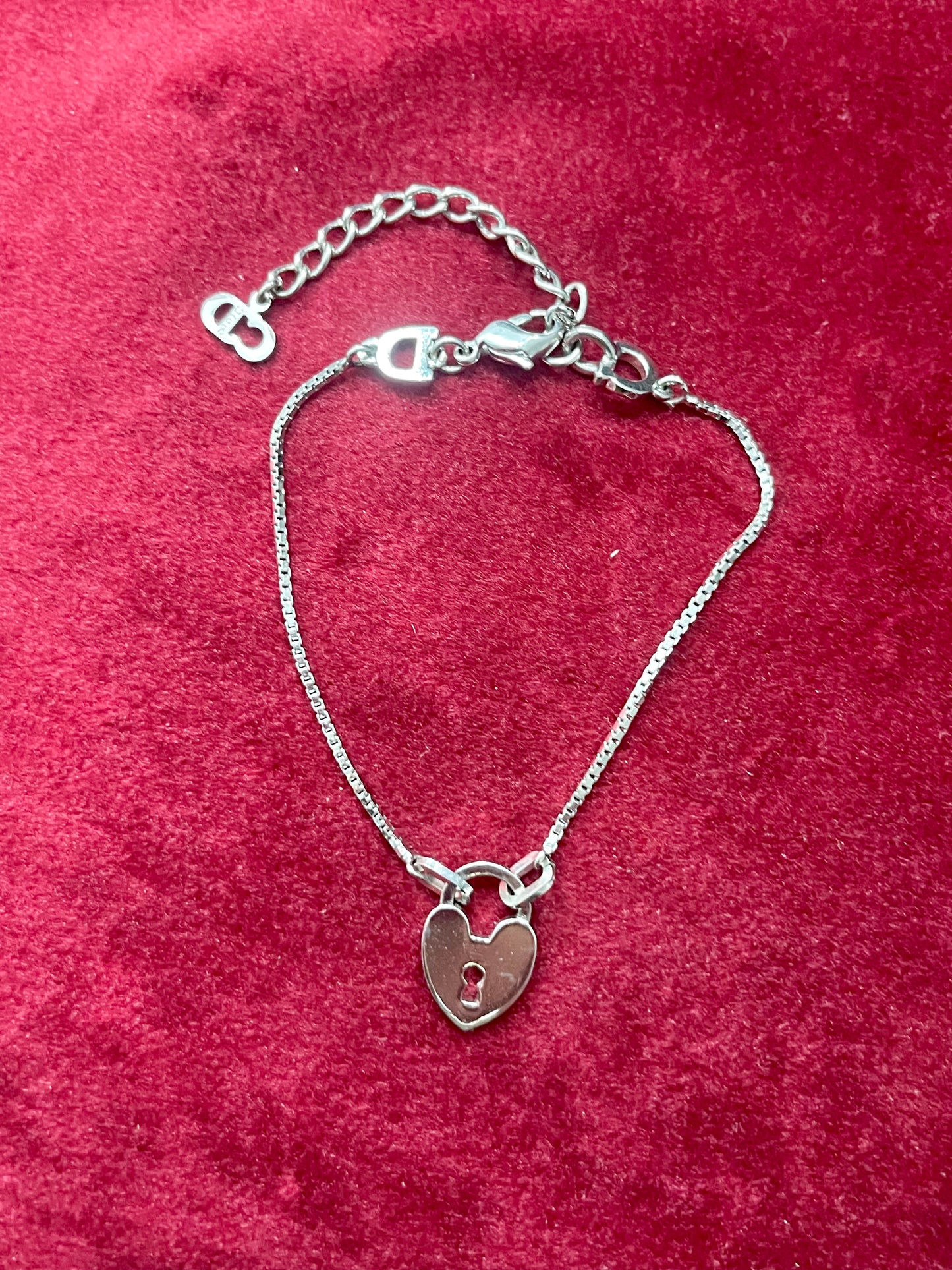 Backside view of Dior silver tone bracelet with a heart -shaped lock pendant on a red textured background