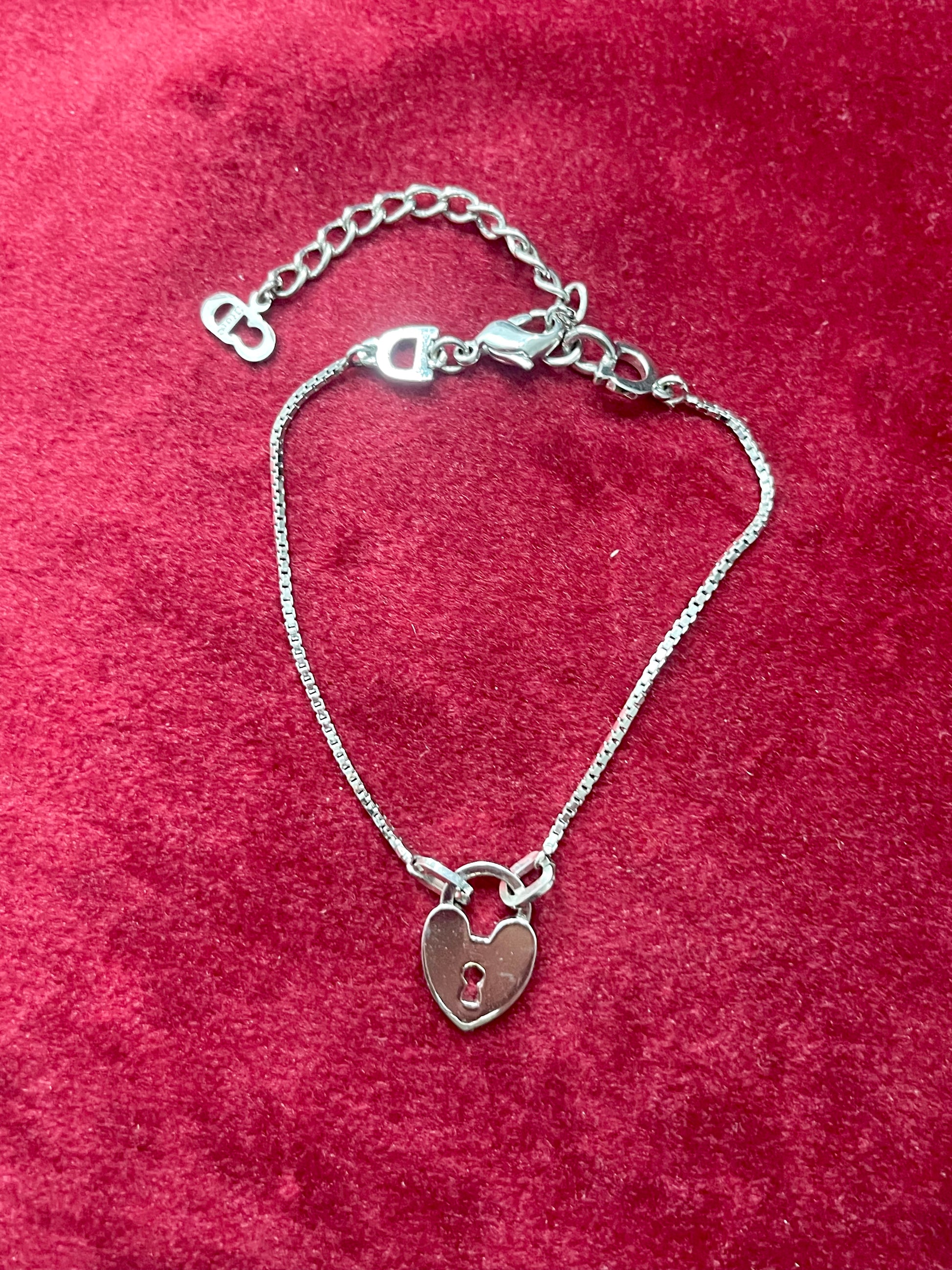 Backside view of Dior silver tone bracelet with a heart -shaped lock pendant on a red textured background