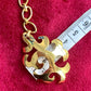 Gold pendant  Yves Saint Laurent upcycled earrings with decorative design on a red background, measured against a ruler.