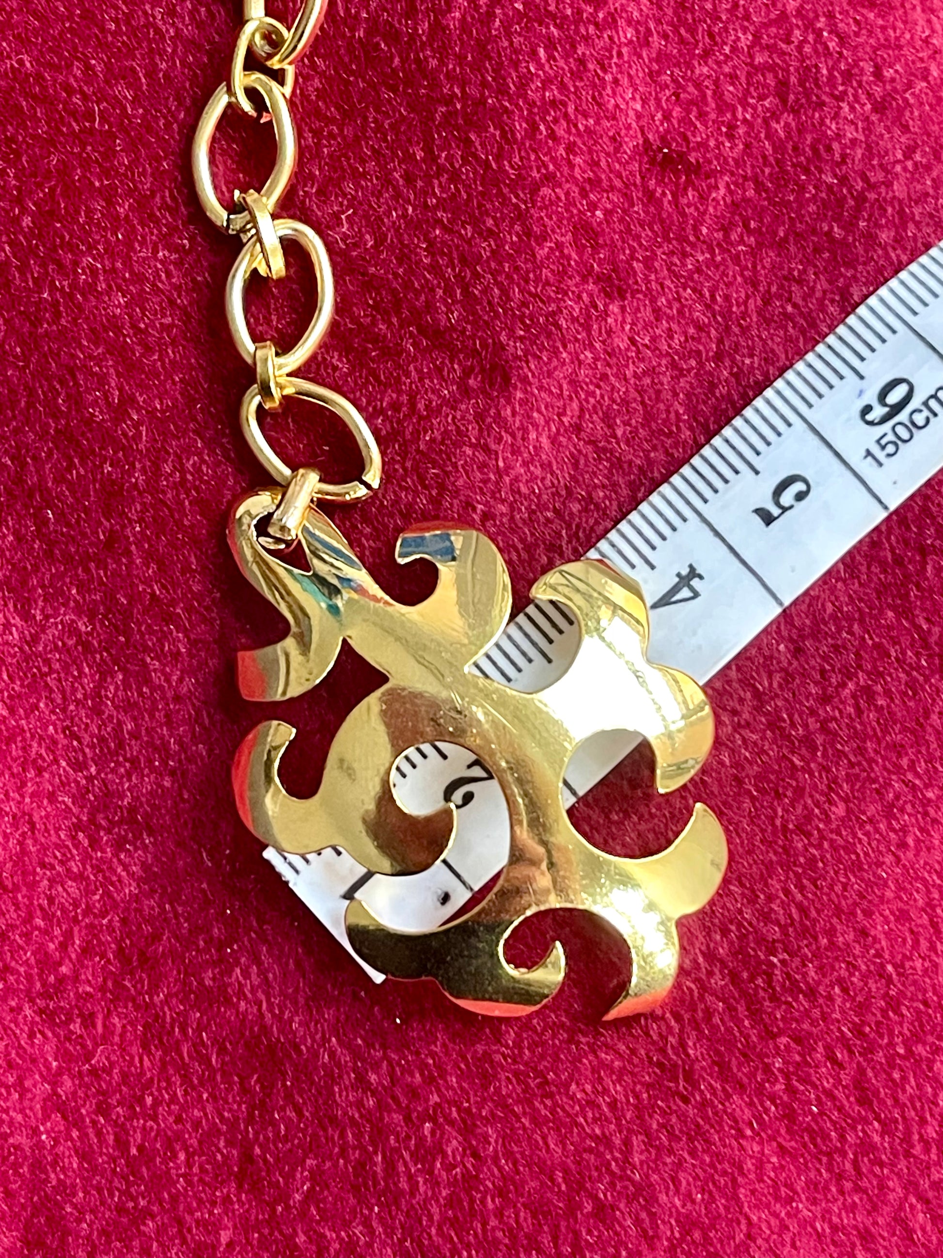 Gold pendant  Yves Saint Laurent upcycled earrings with decorative design on a red background, measured against a ruler.