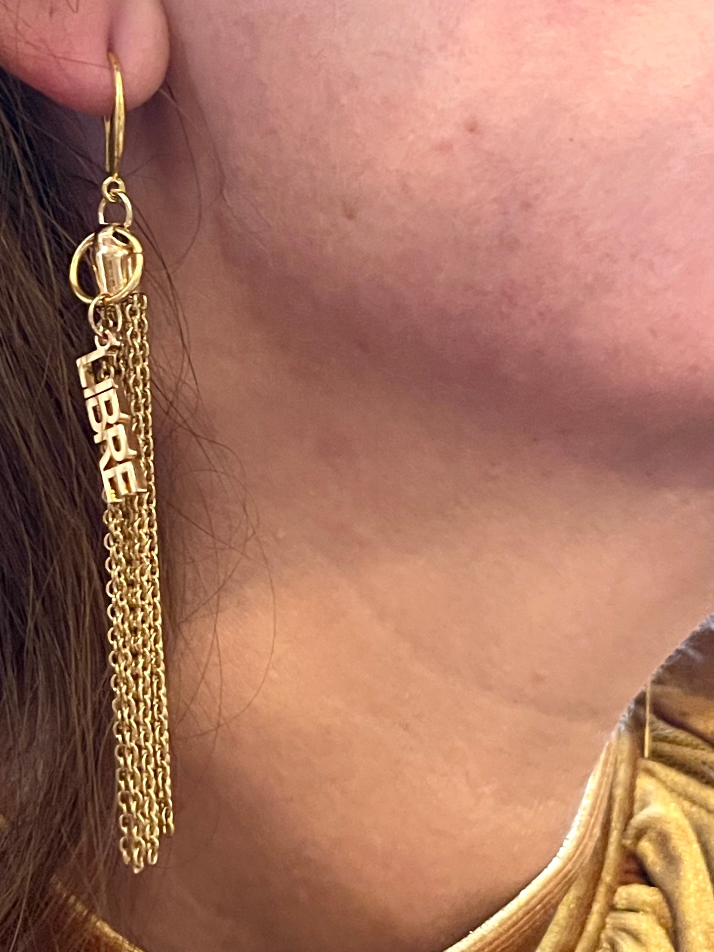 Gold Tassel earring with 'Libre' text worn by a person Yves Saint Laurent 